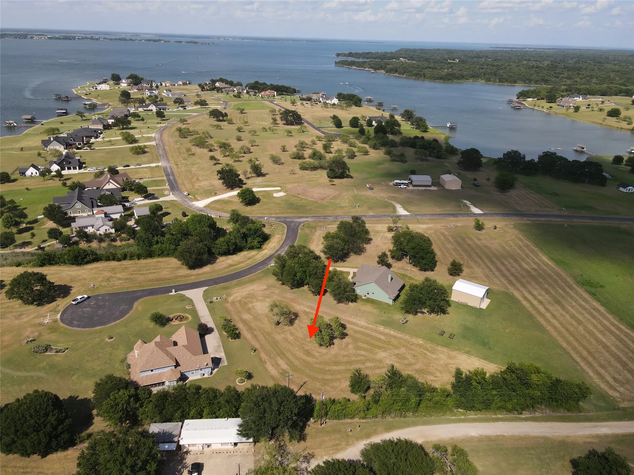 Expansive land parcel featuring open fields and mature trees, situated within a community of residential properties