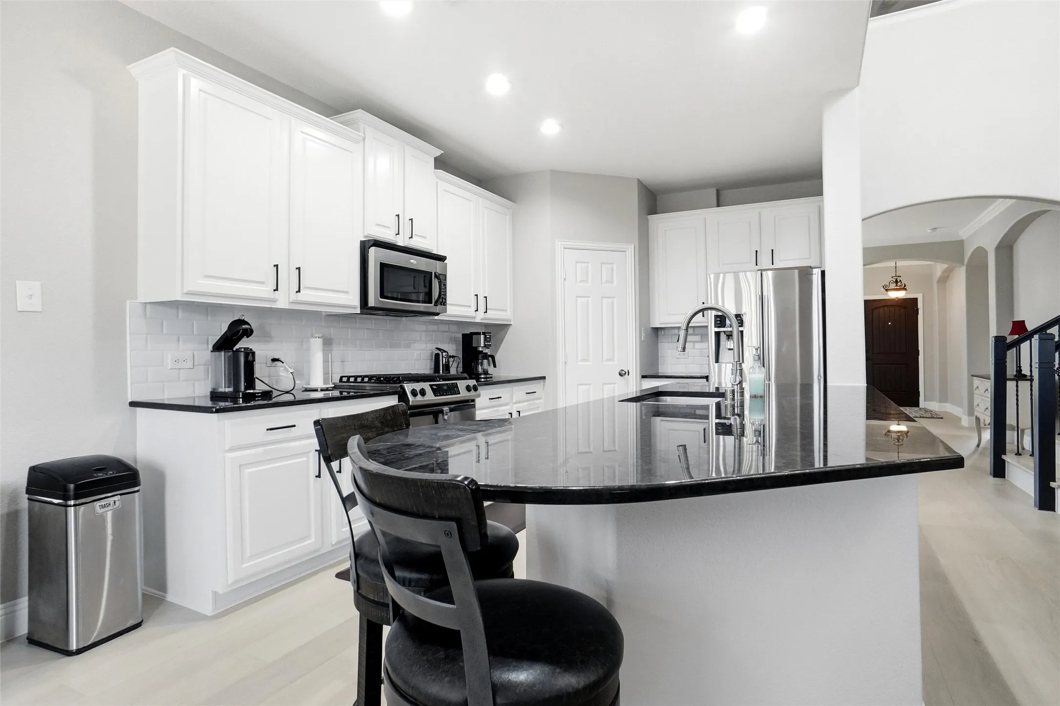 Kitchen featuring a large island with a dark countertop, white cabinetry with black hardware, stainless steel appliances, and a white subway tile backsplash