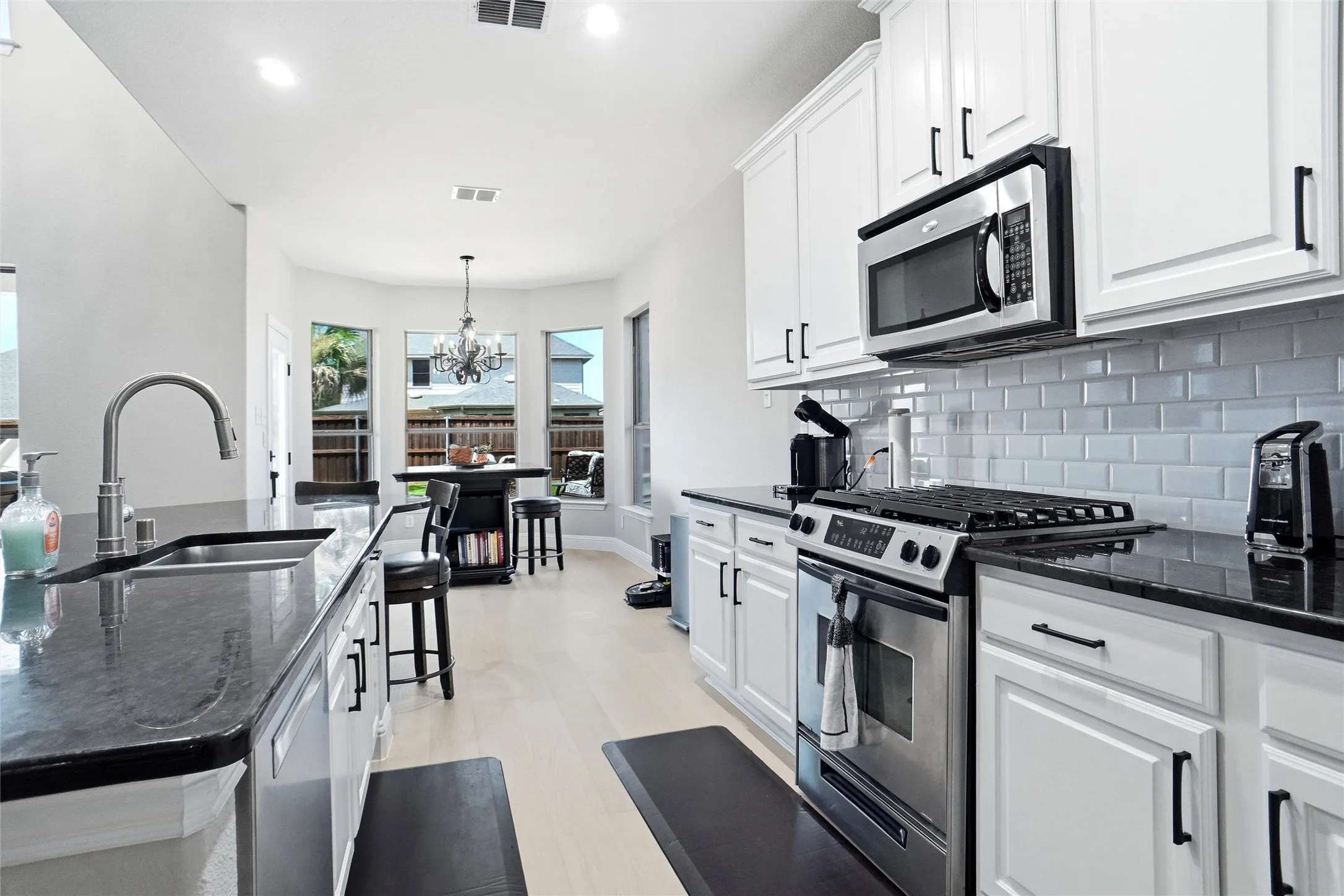 Modern kitchen featuring light wood-finish flooring, white cabinetry with black hardware, dark countertops, a stainless steel gas range, and a subway tile backsplash