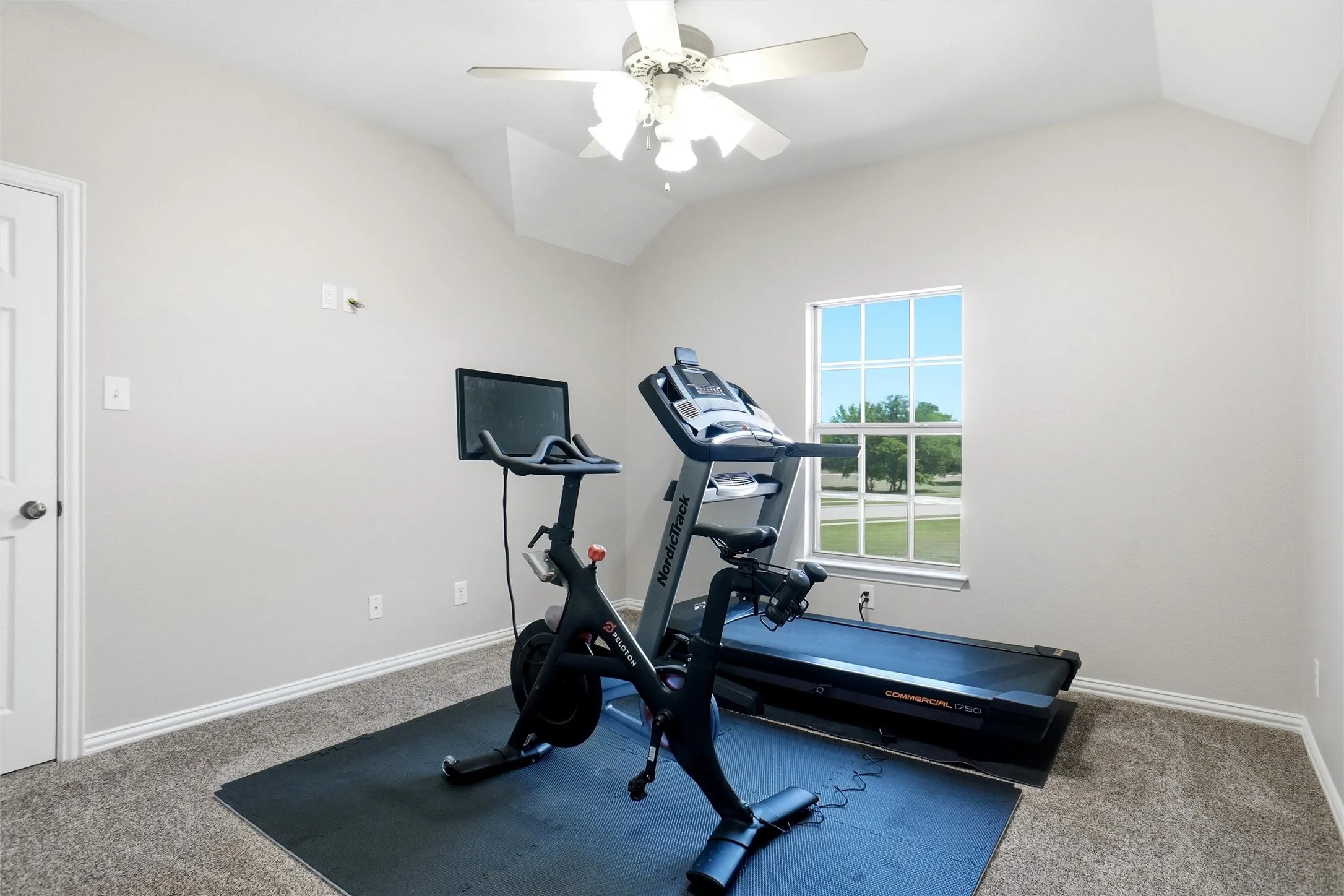 Bright room featuring vaulted ceilings, a ceiling fan, a window with exterior views, and carpet flooring