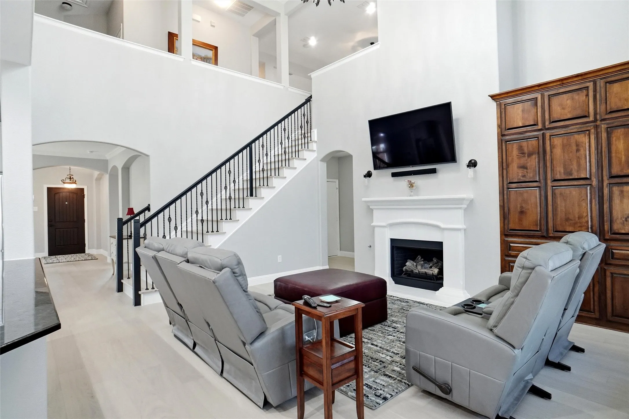 Double-height living area featuring light-toned flooring, a fireplace with a classic white mantel, and extensive built-in wooden cabinetry