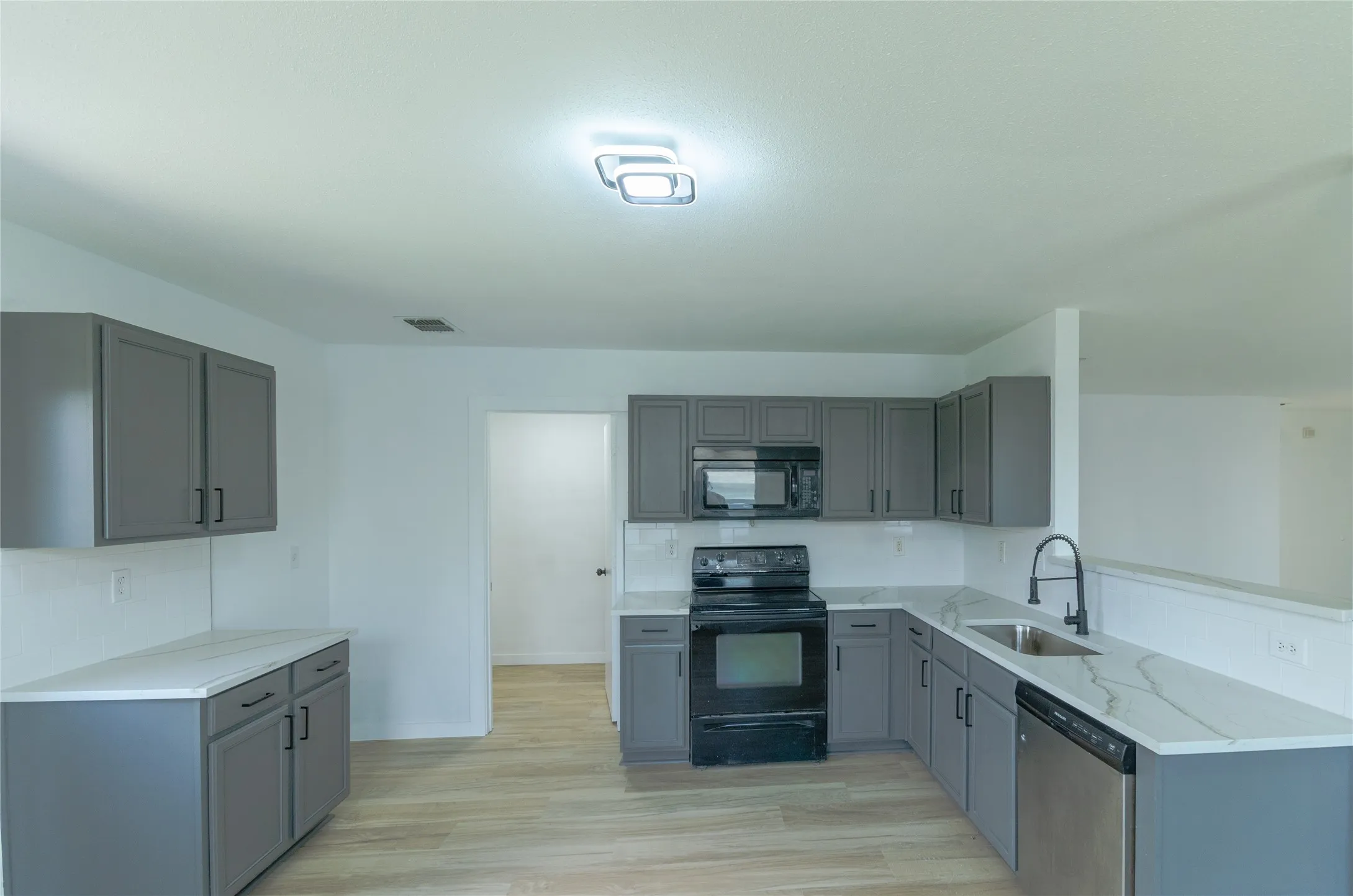 Kitchen featuring gray cabinetry, light countertops, wood-finish flooring, and stainless steel appliances