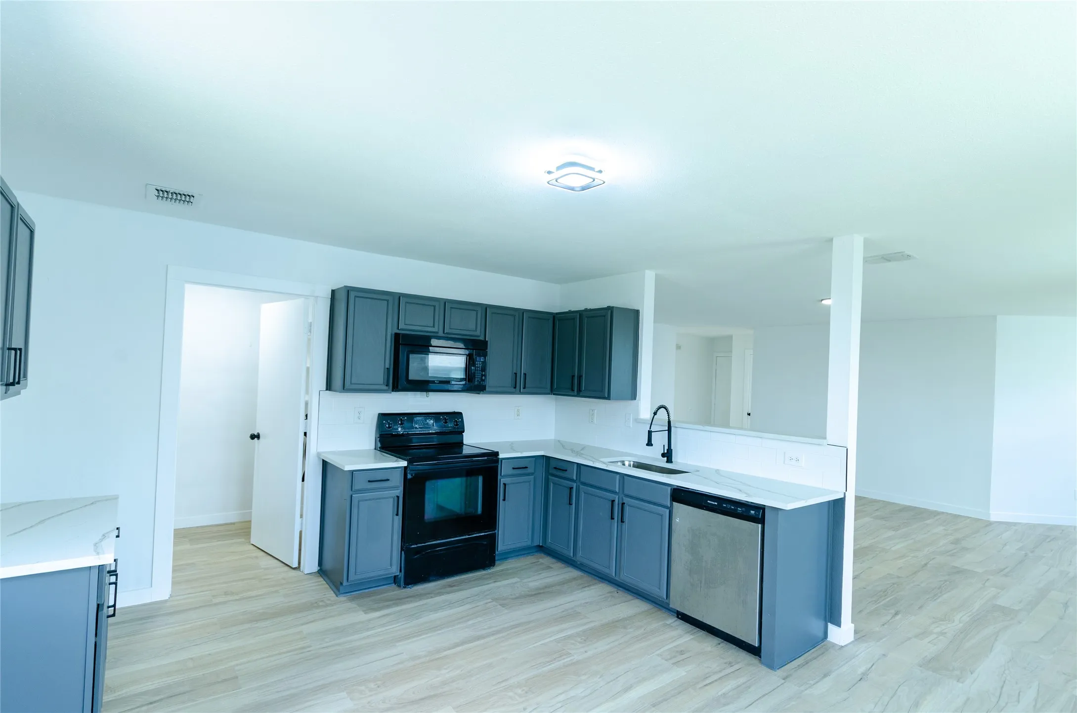 Kitchen featuring a black appliance package, dark gray cabinetry, light-toned countertops, a stainless steel dishwasher, and a matte black faucet