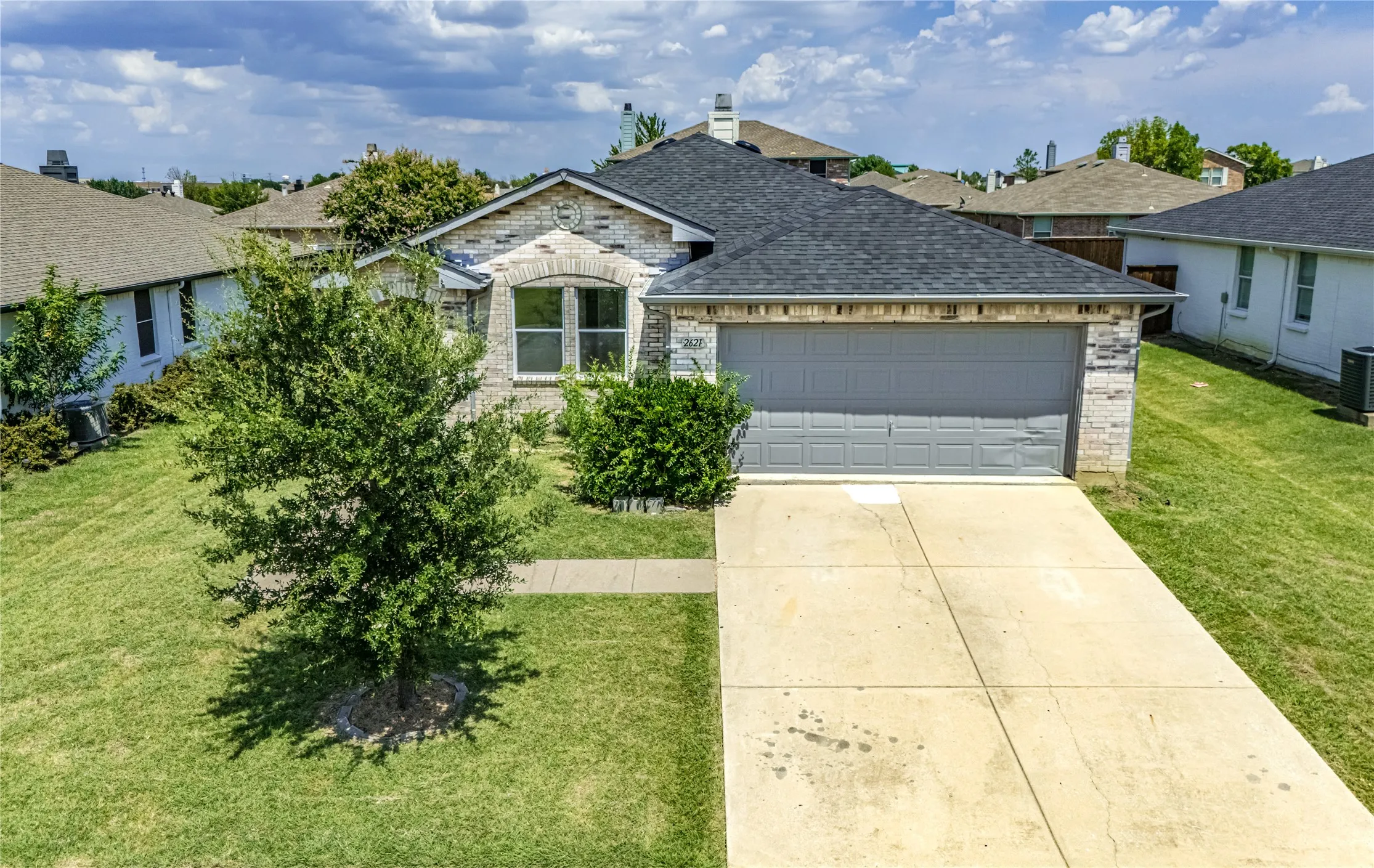 Single-story residence featuring a stone and brick facade, a dark shingle roof, an attached garage with a panel door, a concrete driveway, and a manicured front lawn with mature landscaping