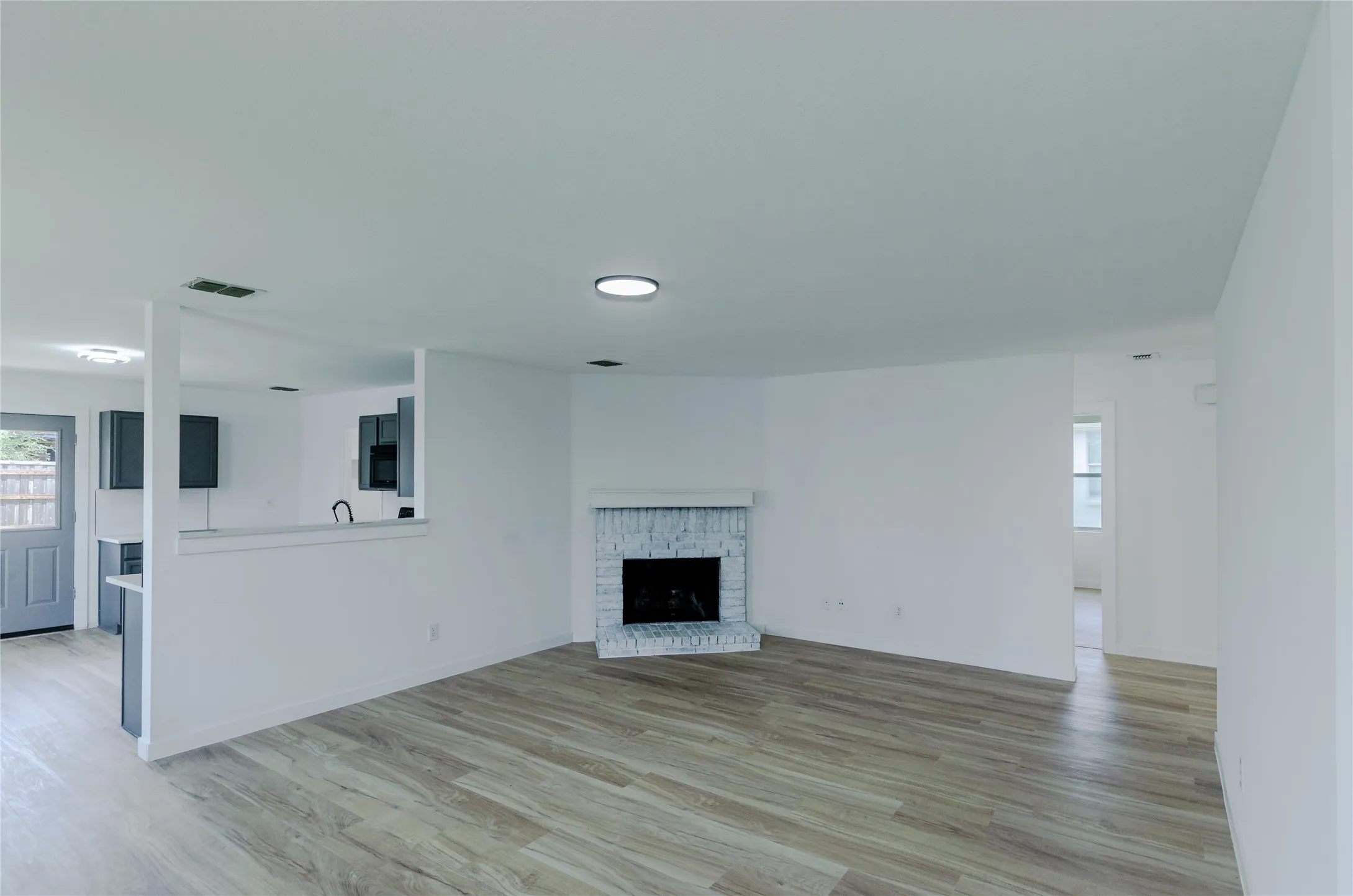 Open-concept living area featuring wood-finish flooring, a painted brick fireplace with a white mantel, and recessed lighting