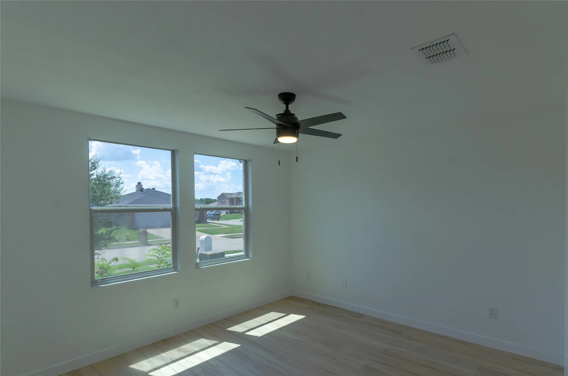 Room featuring two large windows, a ceiling fan with integrated lighting, wood-finish flooring, and white baseboards