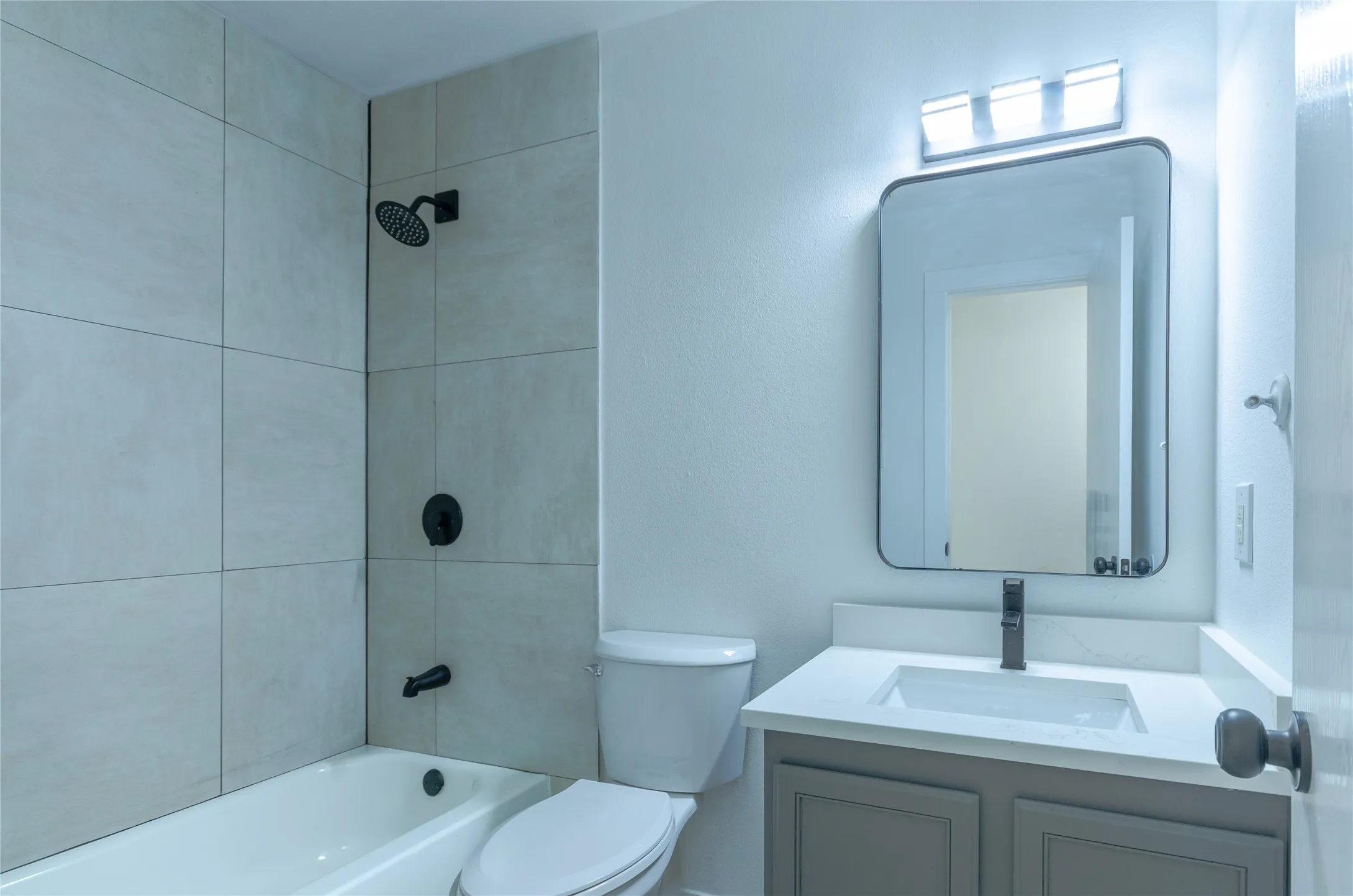 Bathroom featuring a shower-tub combination with large format tile surround, matte black fixtures, a white toilet, and a vanity with a quartz countertop and rectangular sink