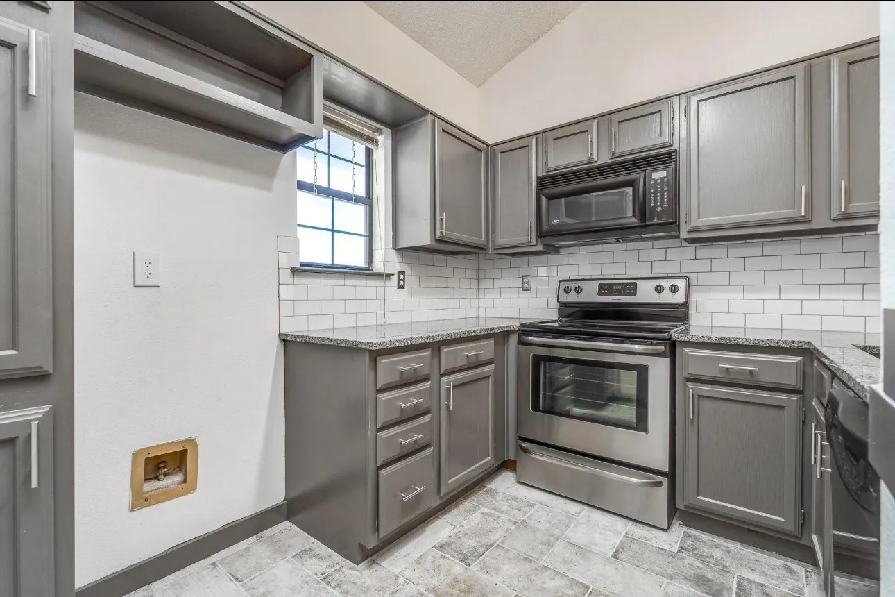 Kitchen with electric stove, dark stone counters, gray cabinets, and backsplash