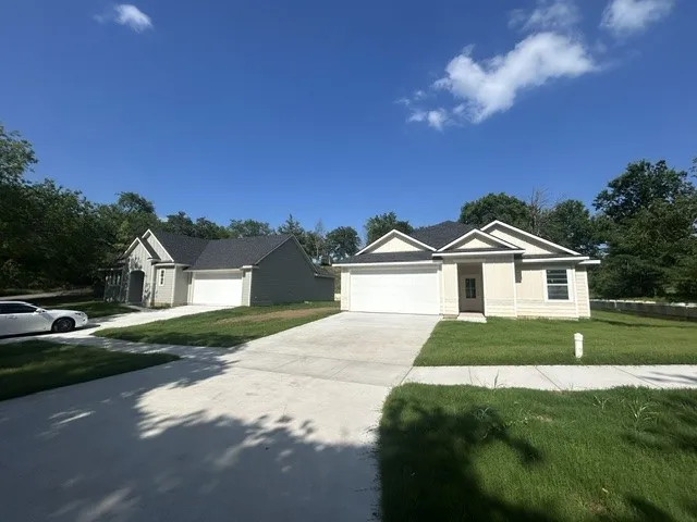 Contemporary residences featuring tan and gray siding, dark shingle roofing, attached two-car garages with white doors, concrete driveways, and green lawns