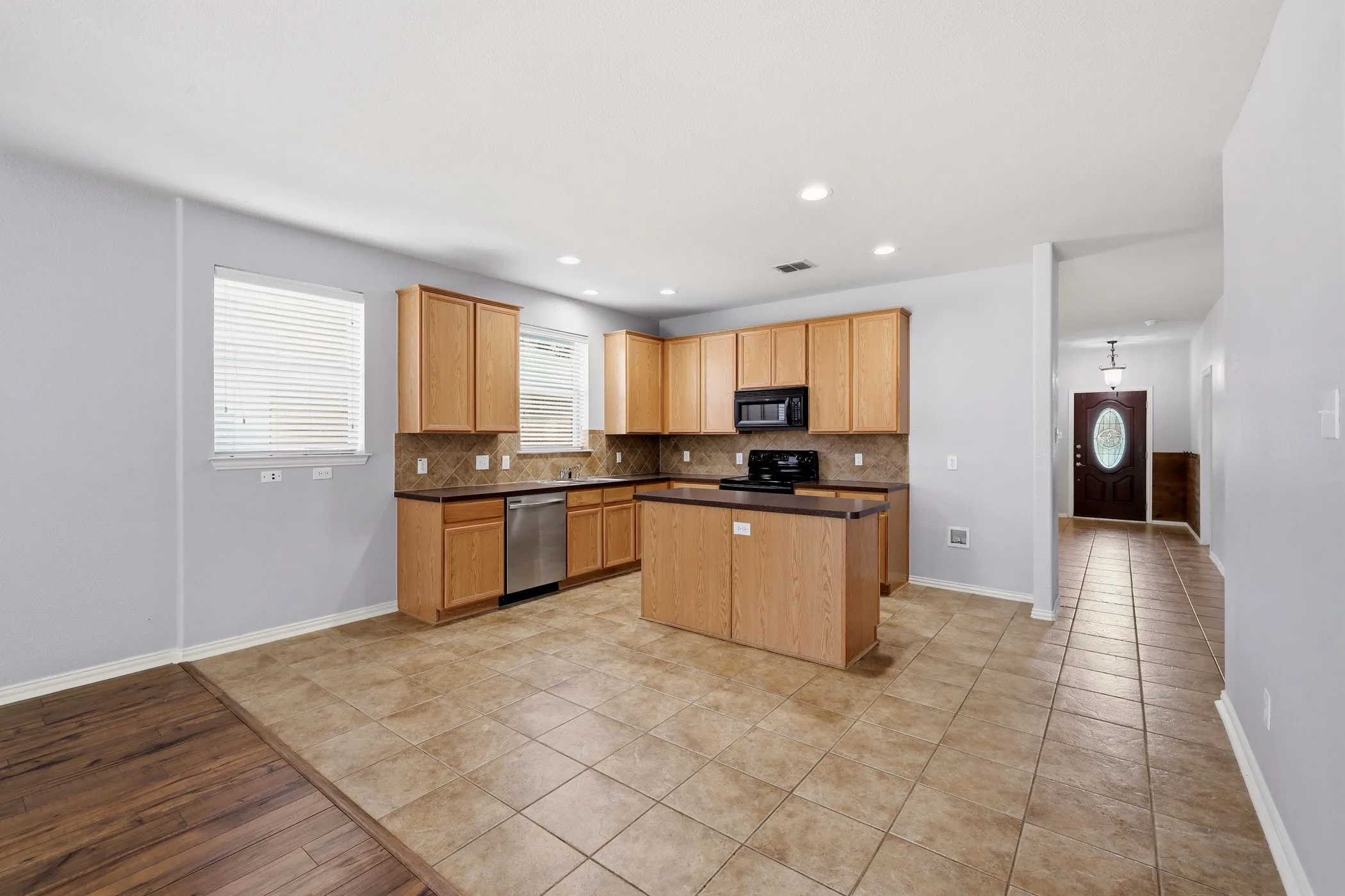 Kitchen featuring wood cabinetry, an island with countertop seating, stainless steel dishwasher, black appliances, and recessed lighting
