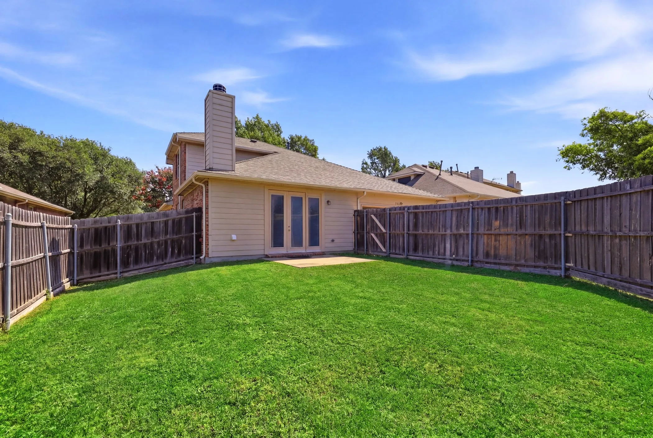 Expansive backyard featuring a lush green lawn, full privacy fencing, and a concrete patio