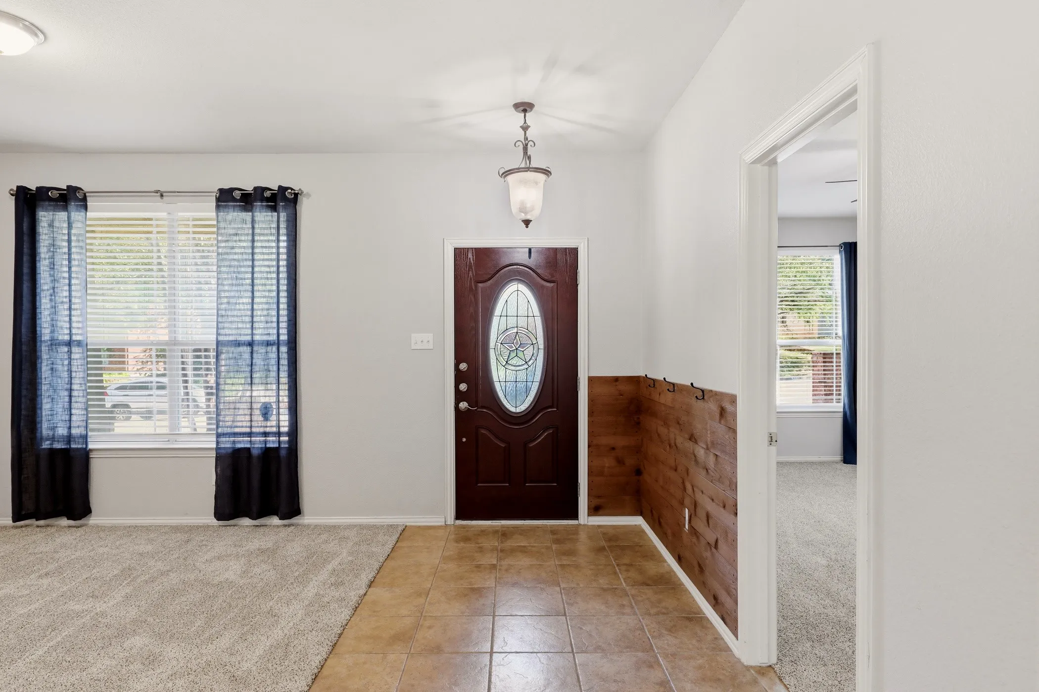 Entryway featuring a decorative front door with an oval glass insert, tile flooring, and wood-paneled wainscoting with coat hooks