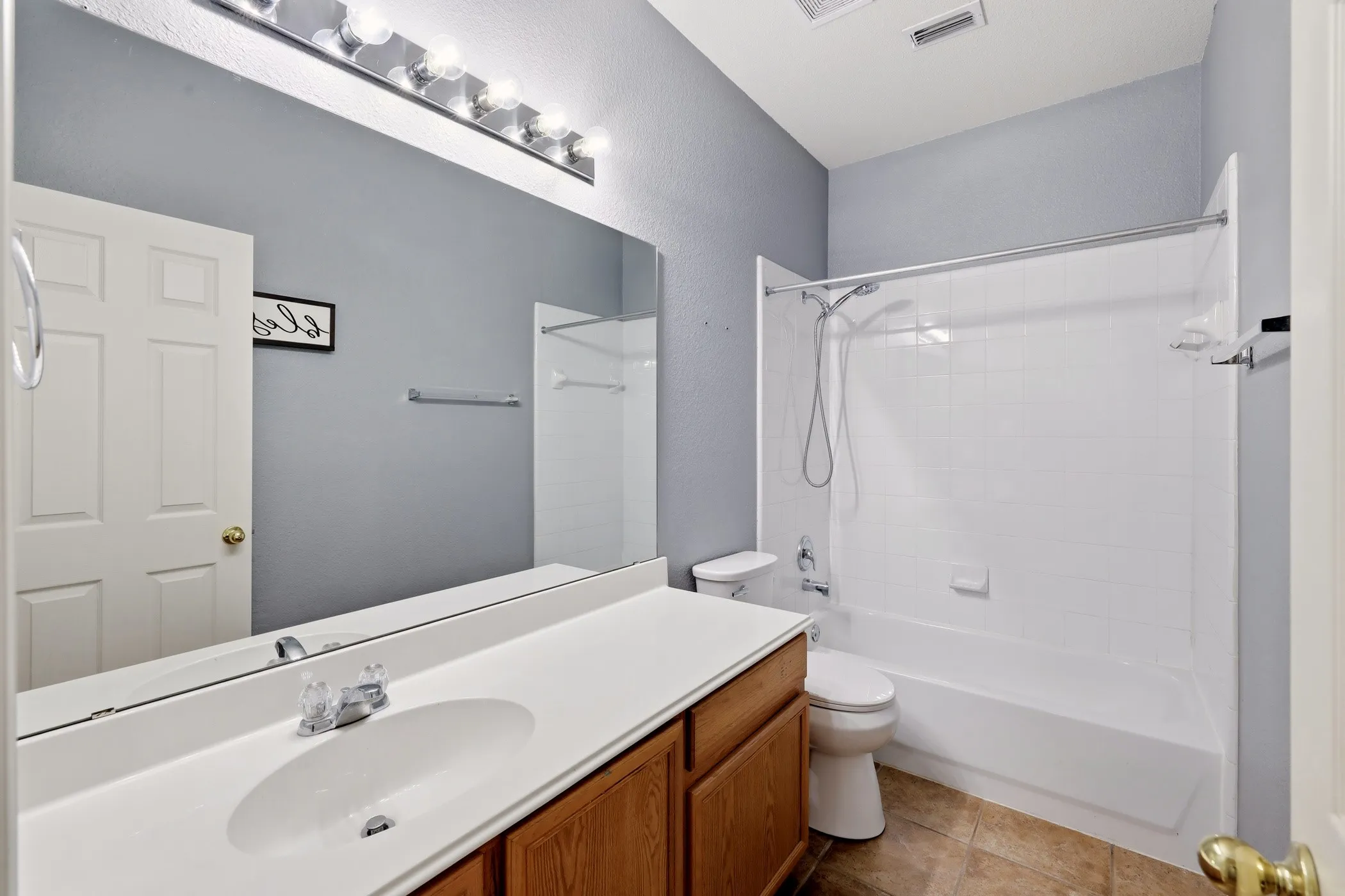 Full bathroom featuring a white tub/shower combination, a wood-finish vanity with an integrated sink, and a large wall-mounted mirror