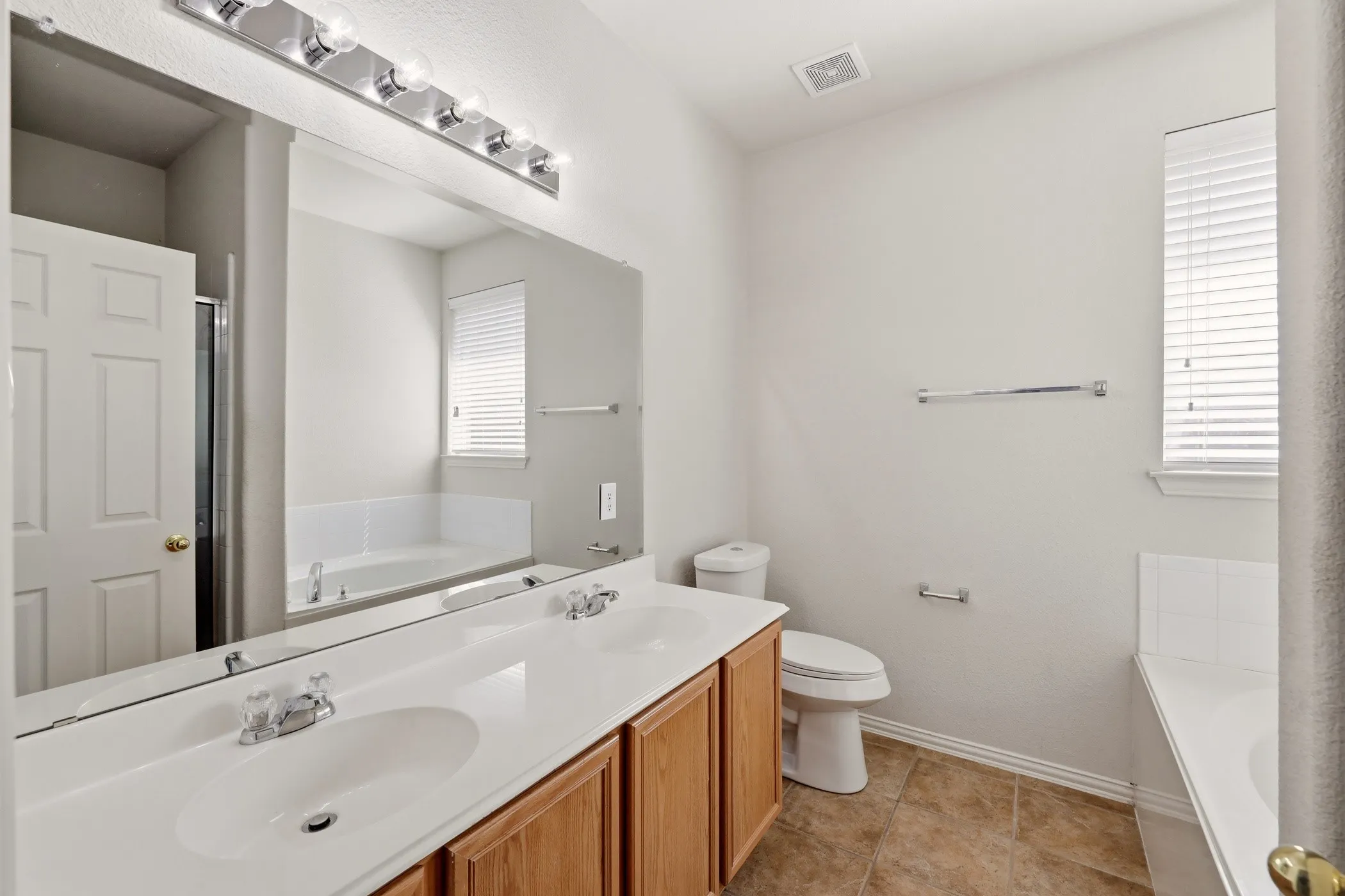 Bathroom featuring a dual vanity with wood-finish cabinetry, a large frameless mirror, a built-in tub, and a separate shower enclosure