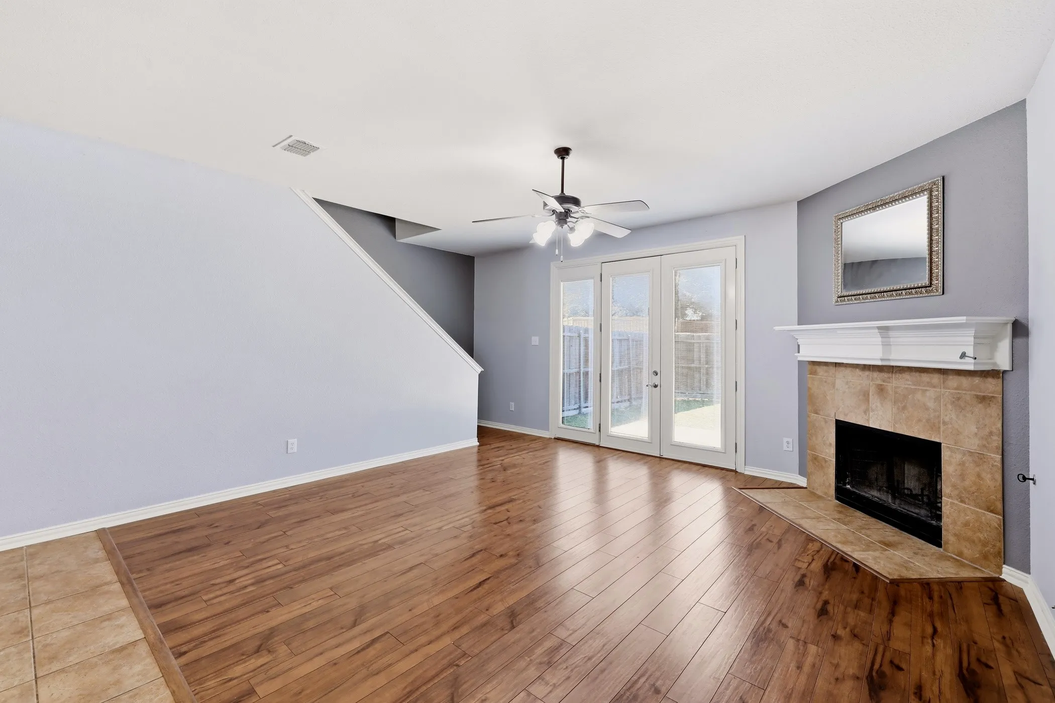 Living area featuring wood-finish flooring, a tile-surround fireplace with a white mantel, and French doors