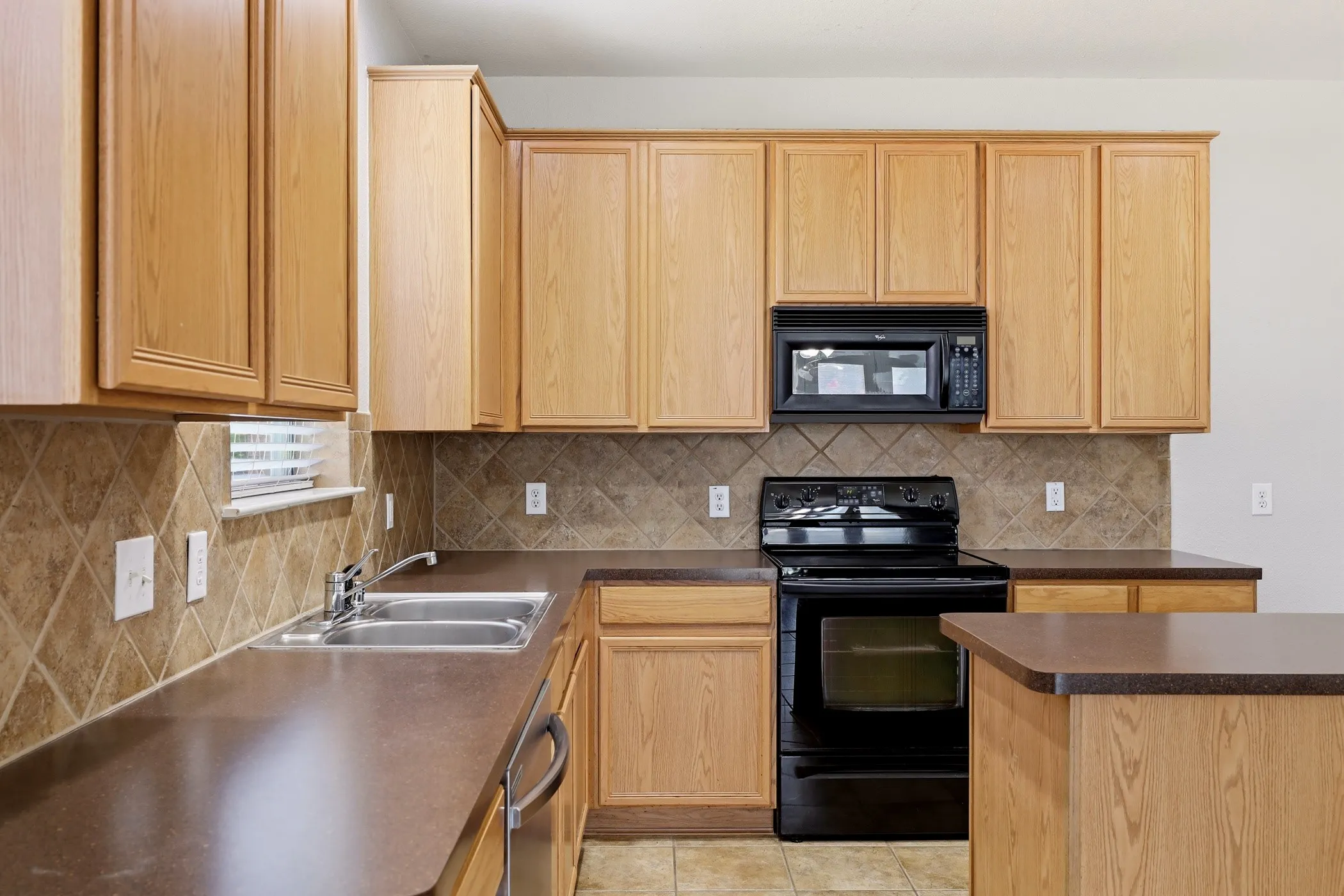 Open-concept kitchen featuring light wood-finish cabinetry, solid surface countertops, and a full suite of black appliances, including a built-in microwave