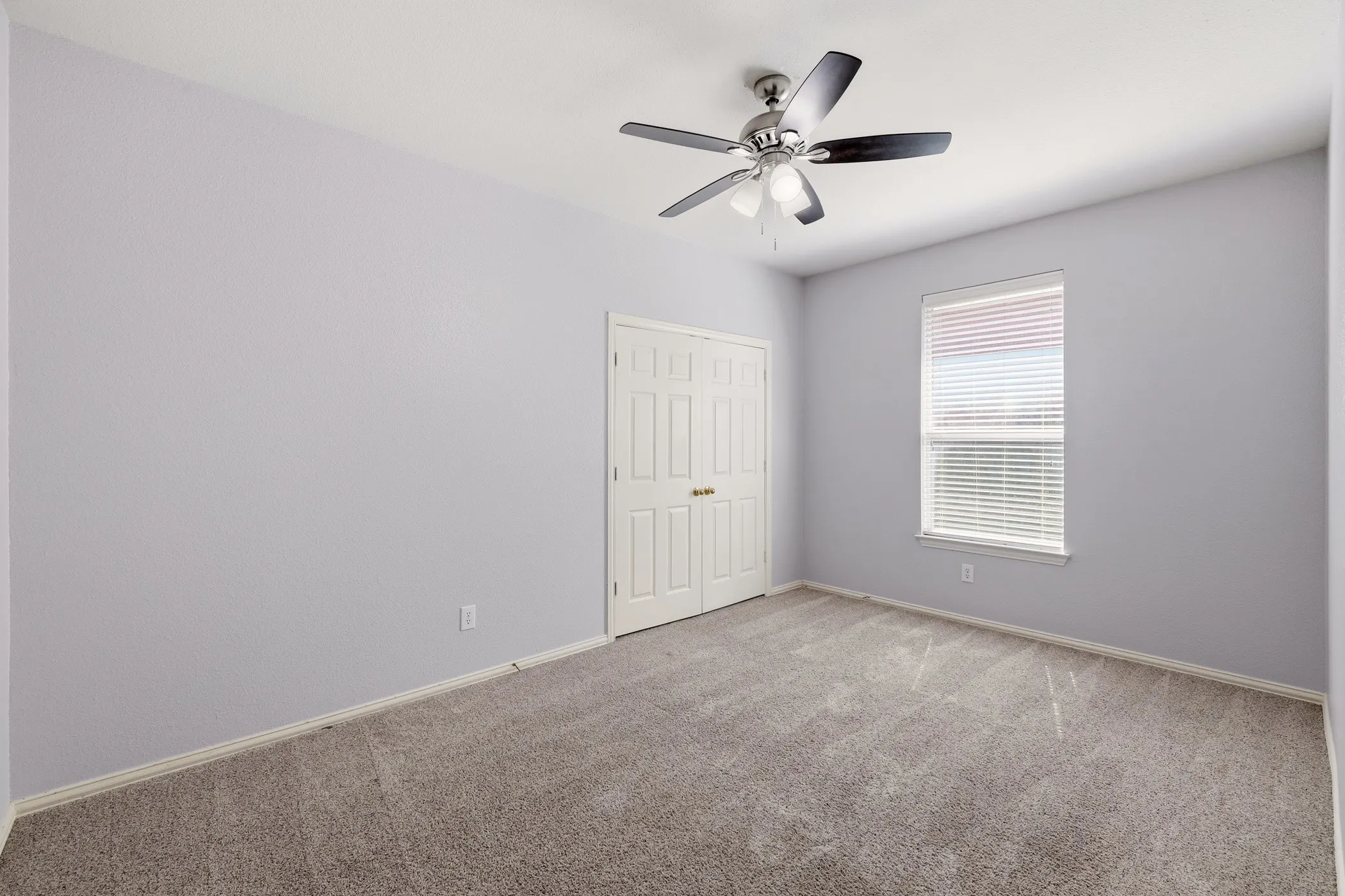 Carpeted room featuring a ceiling fan with light fixture, window with blinds, and white bi-fold closet doors