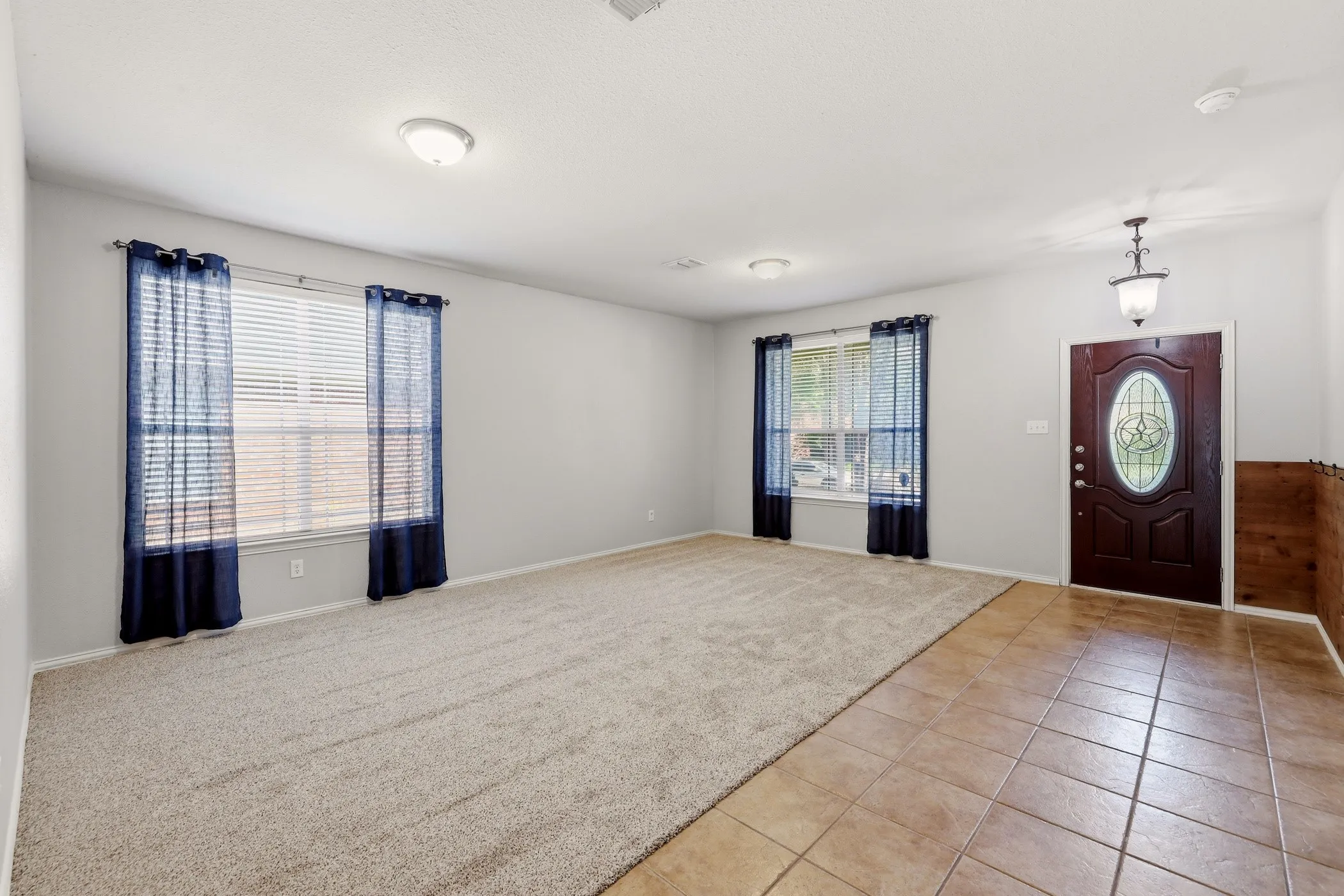 Spacious entry hall featuring ceramic tile flooring, a dark wood entry door with oval glass insert, and a traditional hanging light fixture