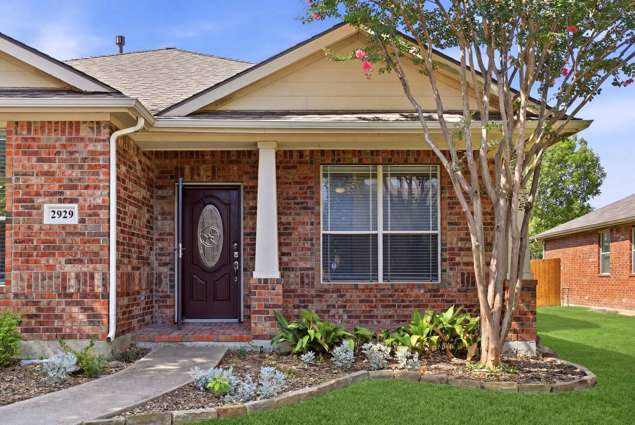 Brick exterior with a covered entry, featuring a dark wood front door with an oval glass insert