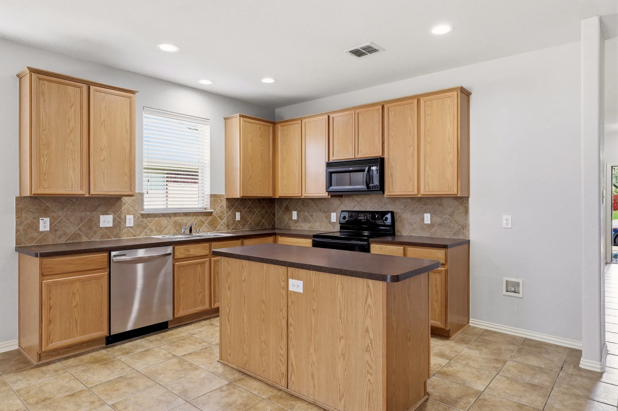 Open-concept kitchen featuring wood-finish cabinetry, a central island, tile flooring, and a tile backsplash