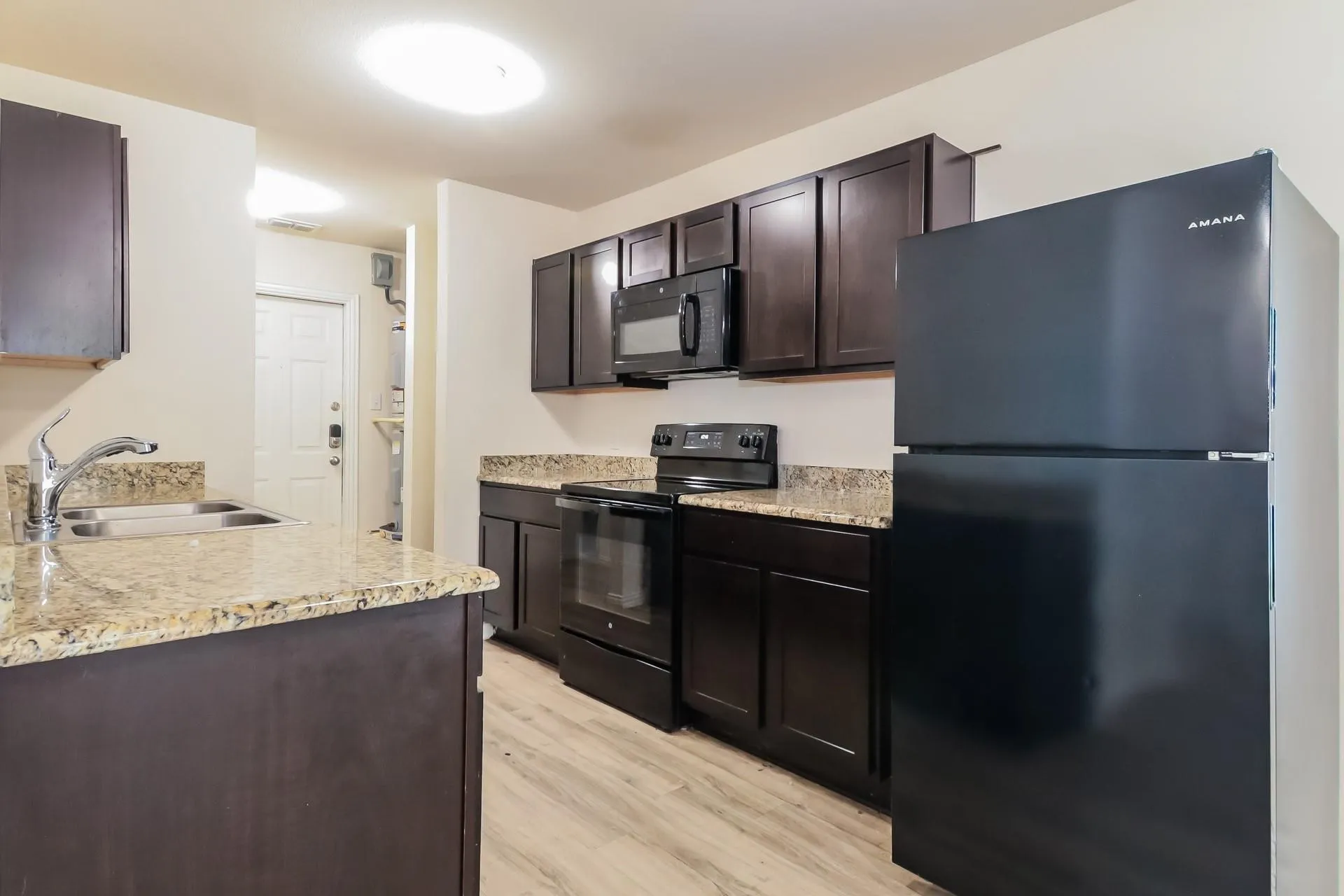 Kitchen featuring dark wood-finish cabinetry, light speckled countertops, and wood-finish flooring