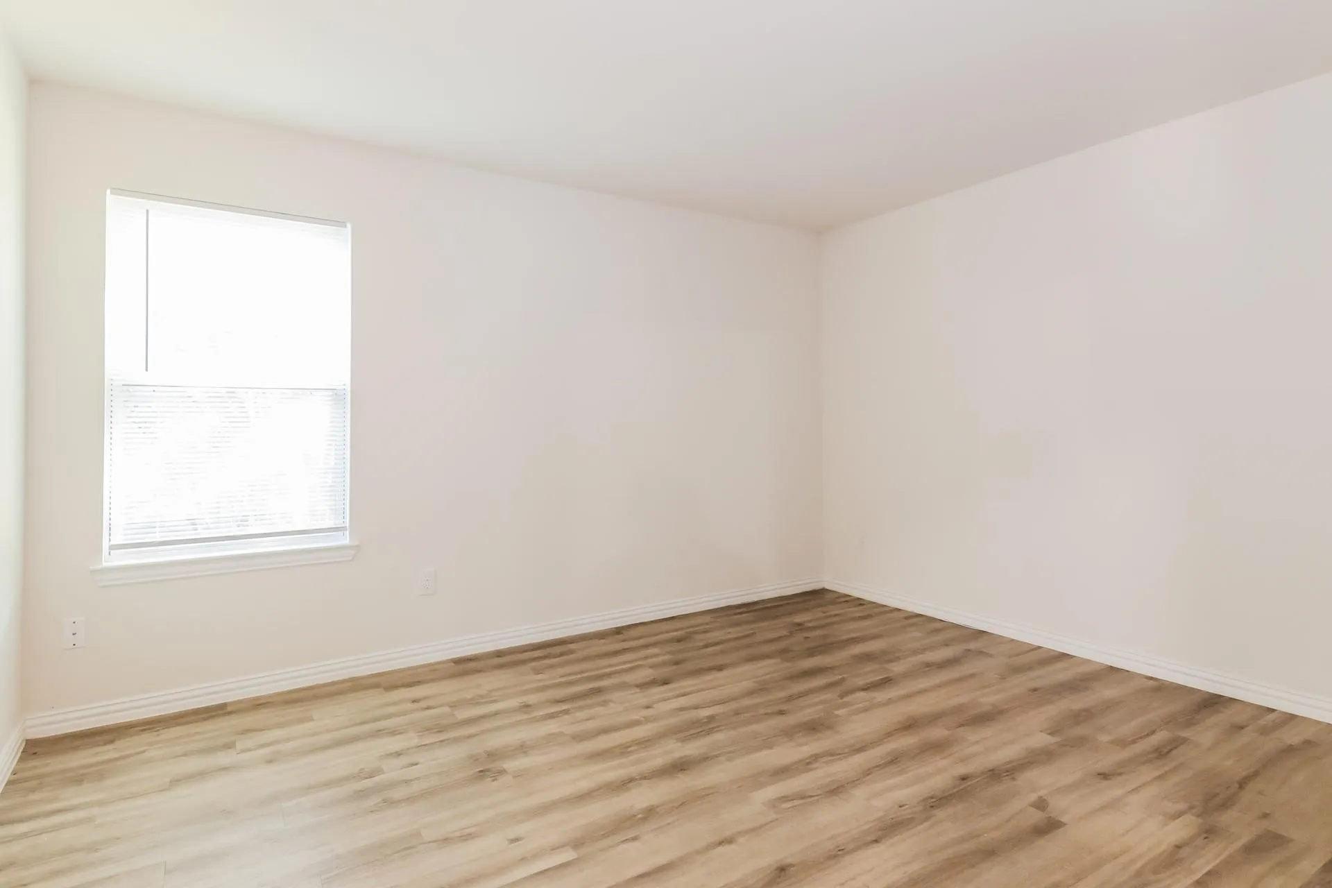 Bright interior room featuring a window with integrated blinds, wood-finish flooring, white baseboards, and neutral wall paint