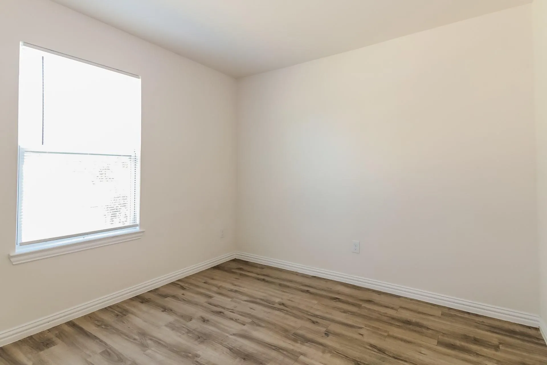 Room with wood-finish flooring, light-toned walls, and a window featuring blinds