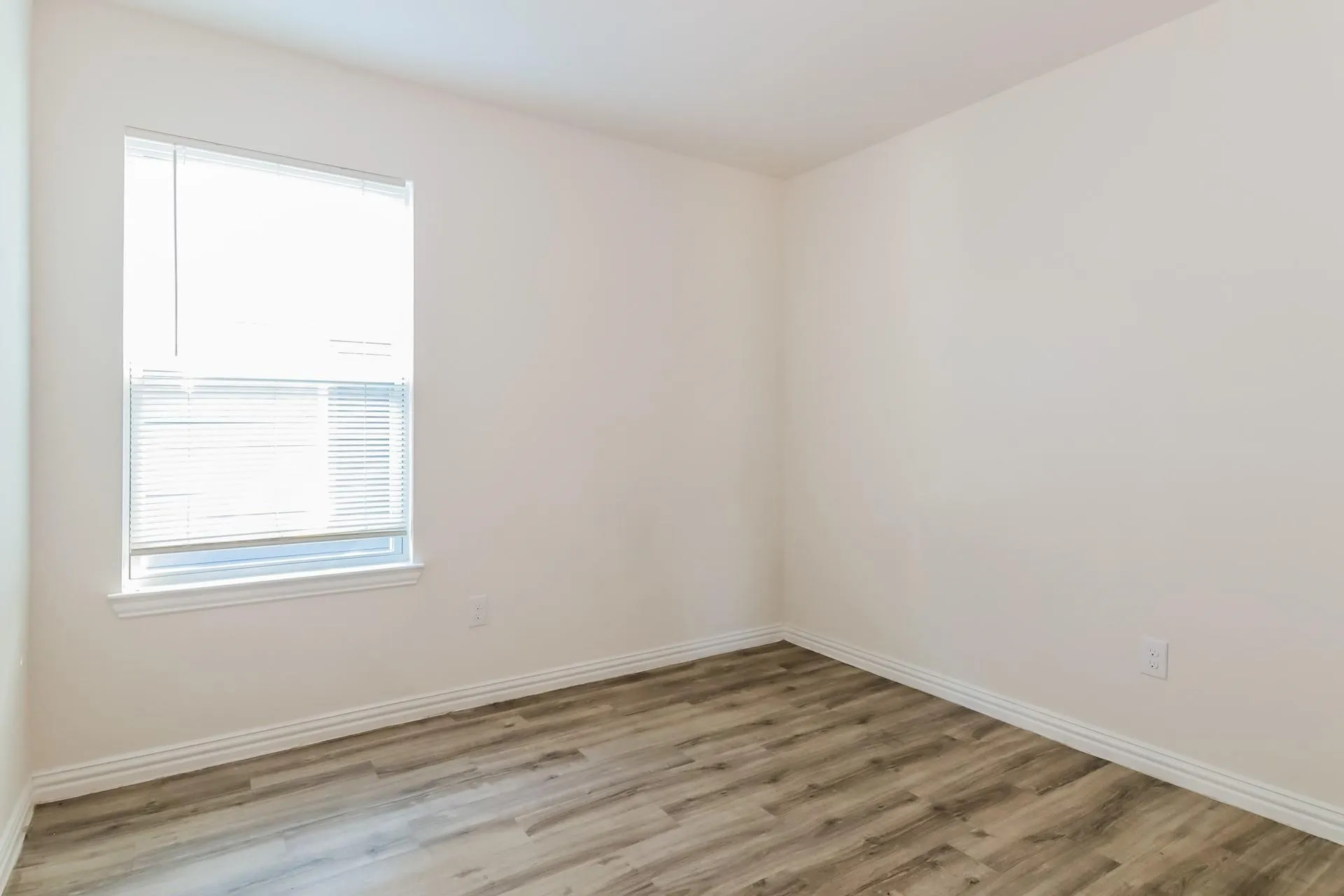 Room featuring light-colored walls, wood-finish flooring, white baseboards, and a window with blinds