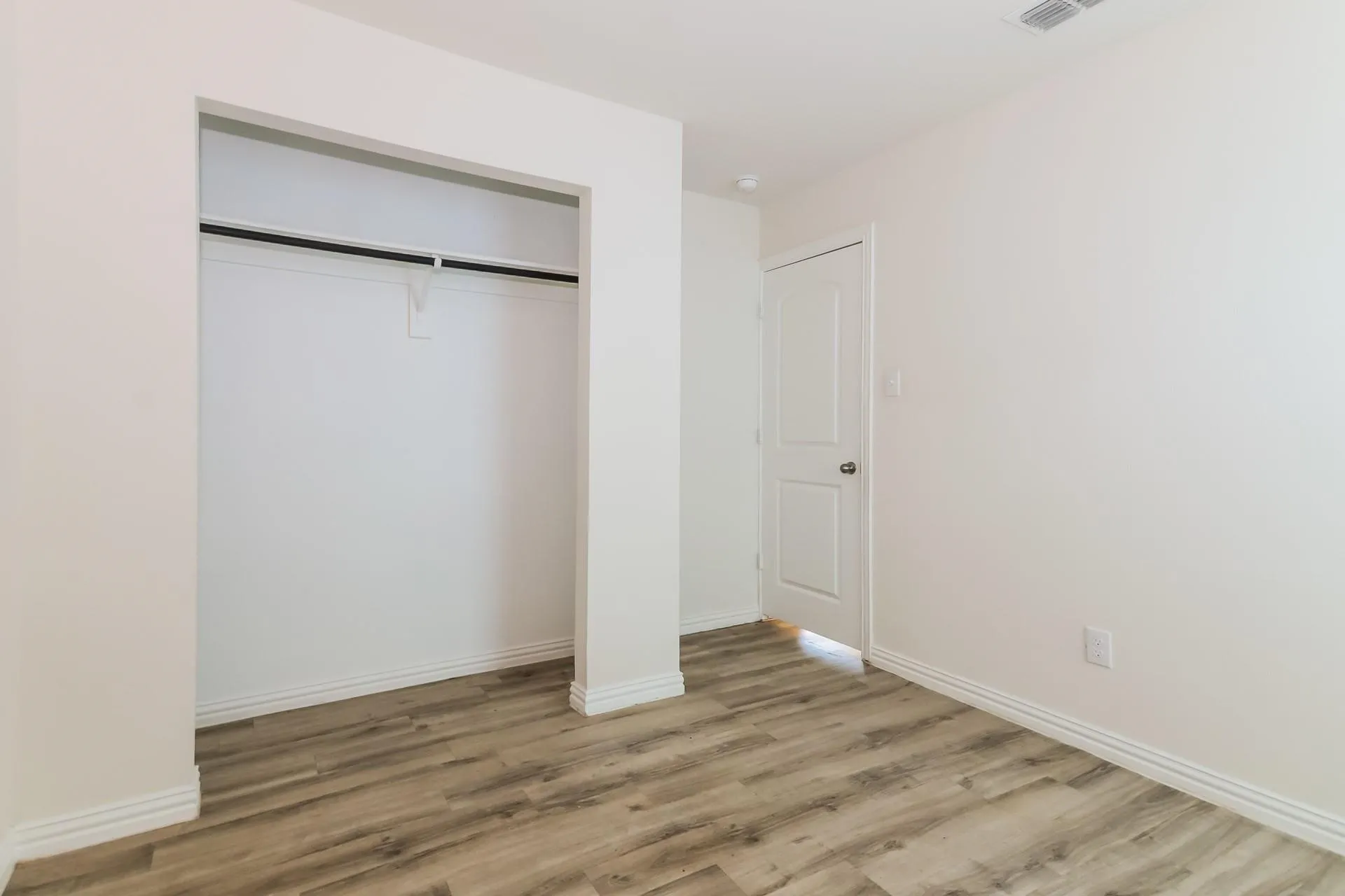 Room featuring wood-finish flooring, a built-in closet with hanging rod, white baseboards, white walls, and a white interior door