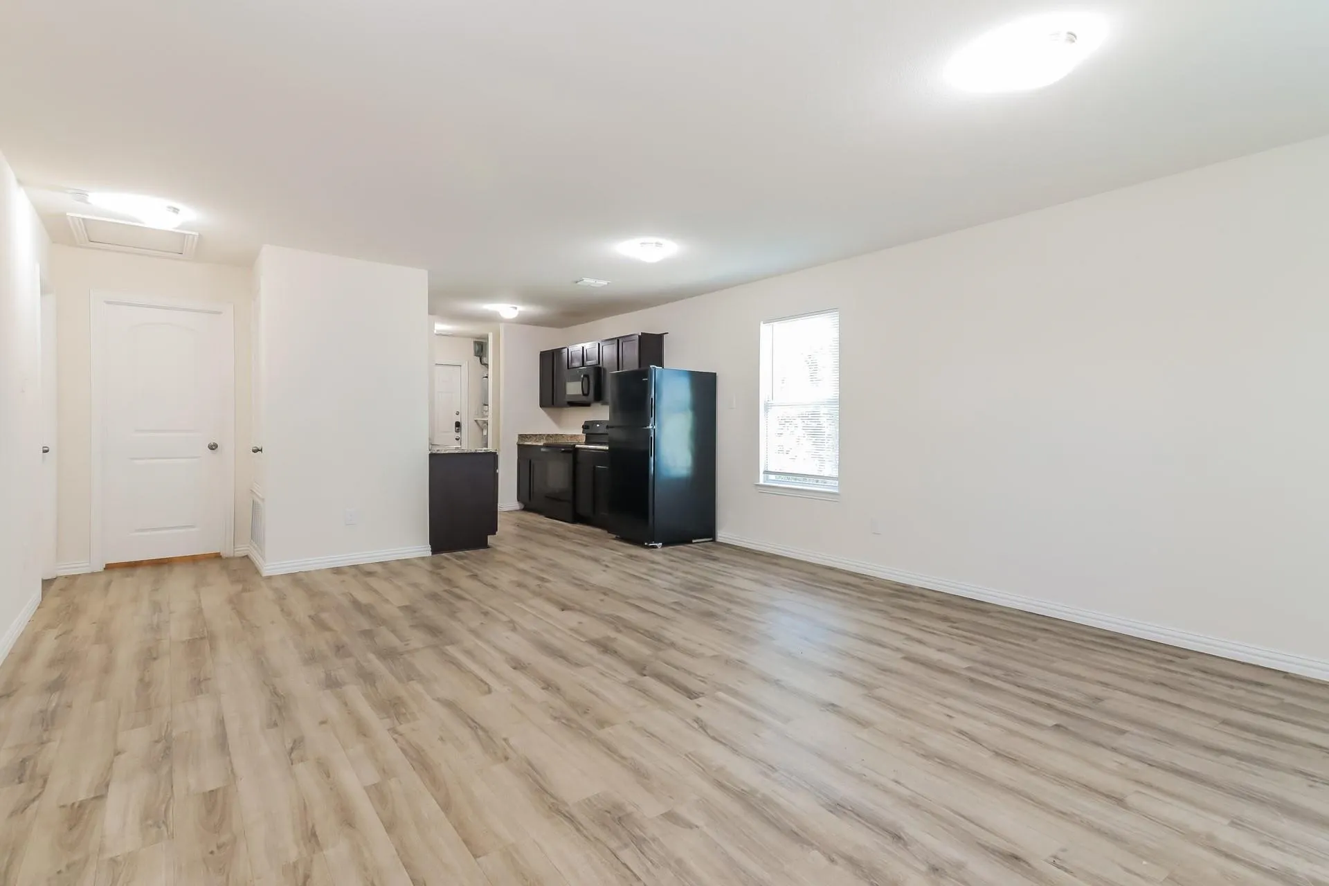 Expansive open-concept room featuring light wood-finish flooring and white walls