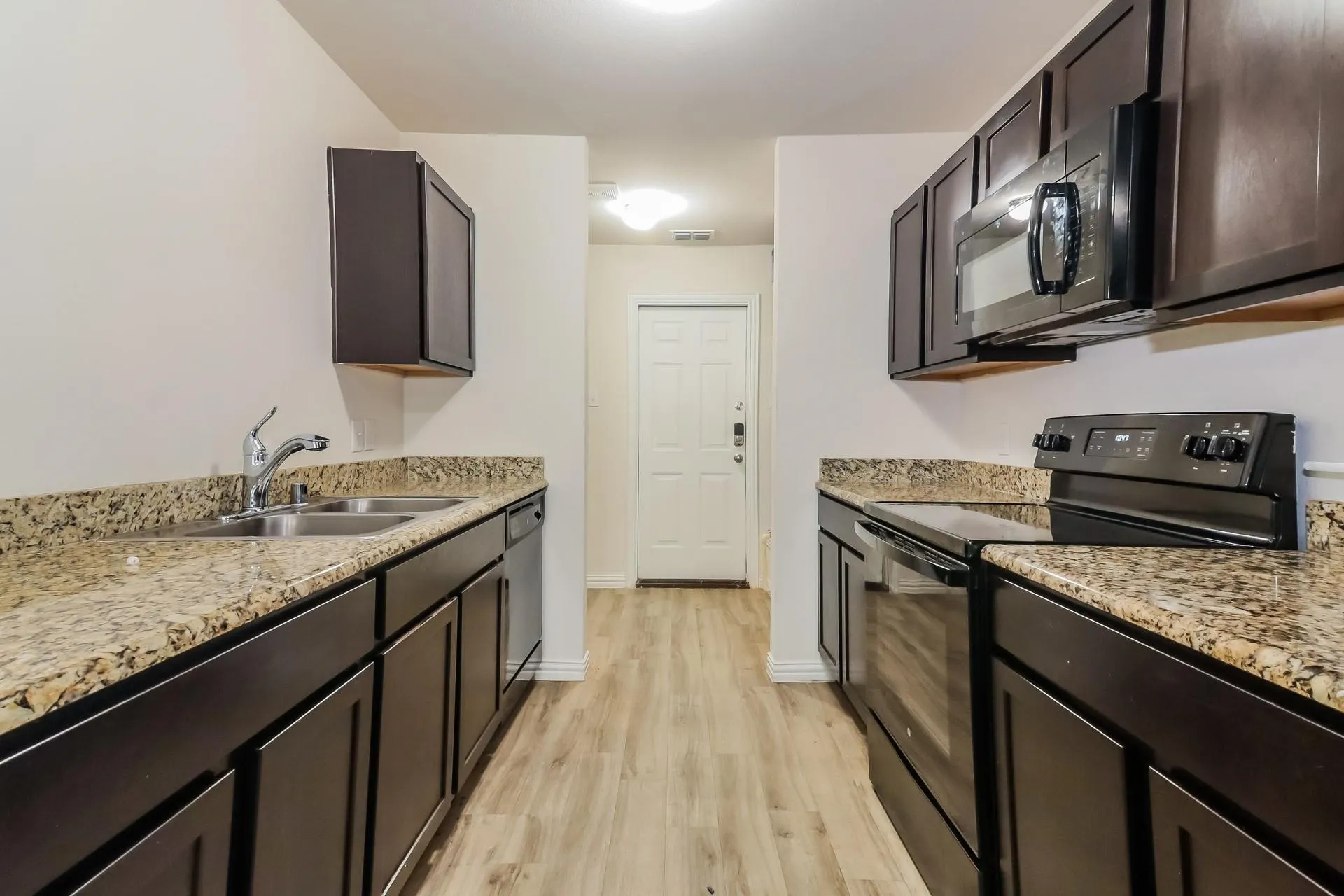 Galley kitchen featuring dark wood cabinetry, light-toned granite-style countertops, and wood-finish flooring