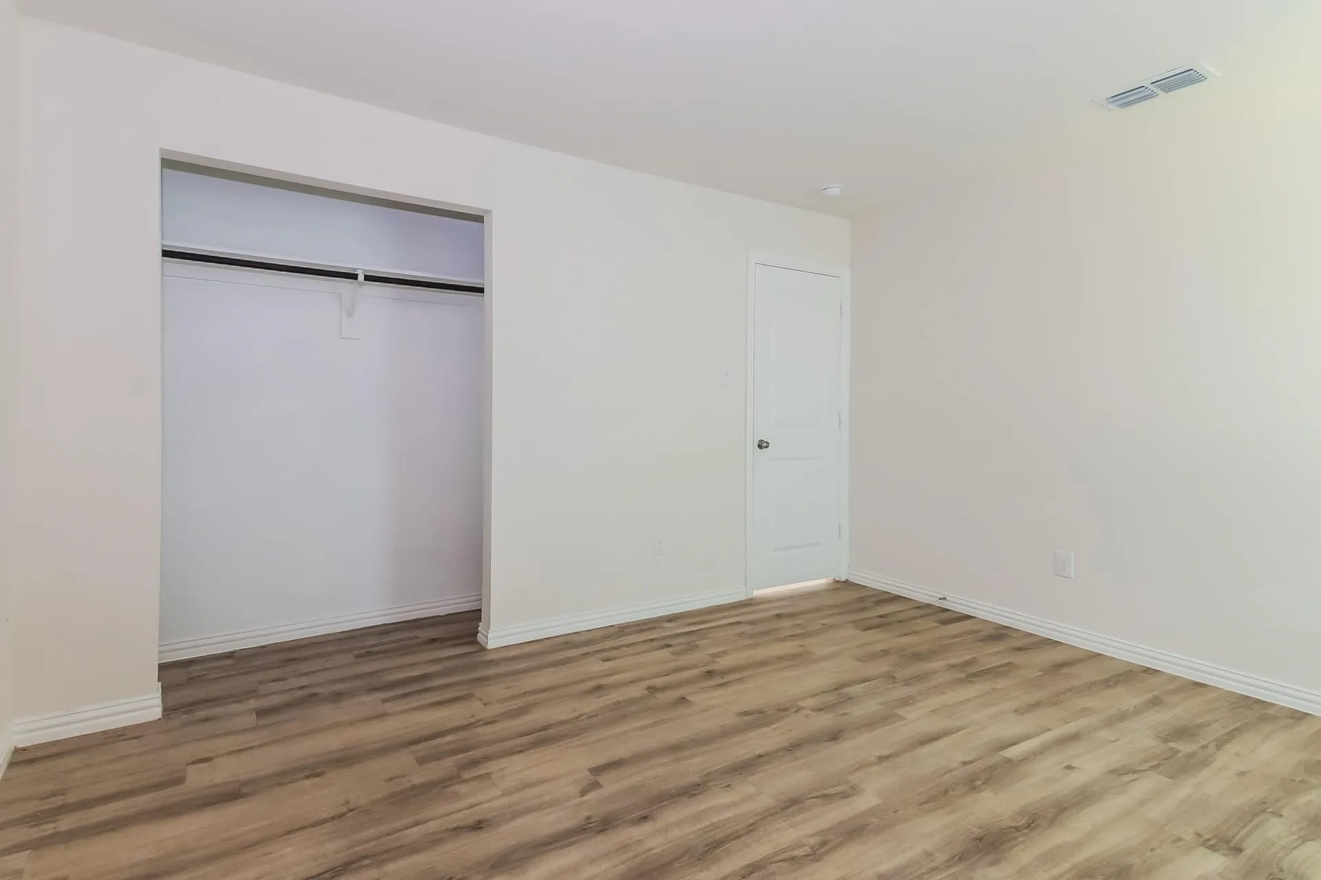 Room featuring wood-finish flooring, white baseboards, and a recessed clothing rod