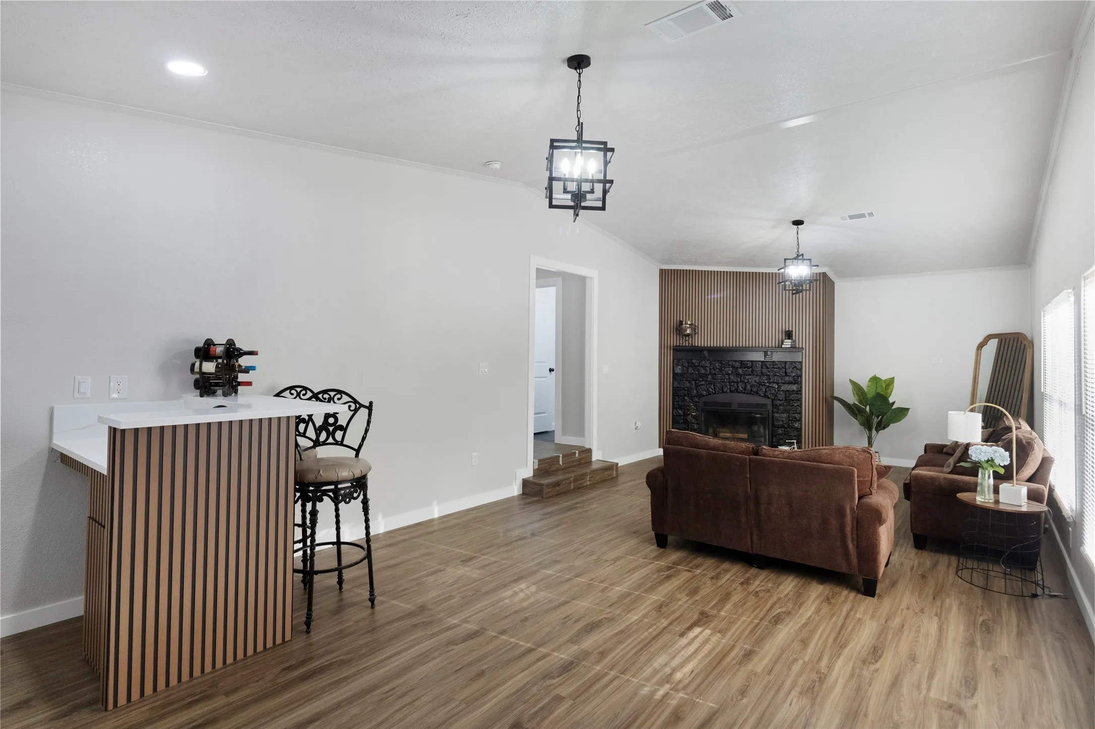Spacious living area featuring wood-finish flooring, a modern fireplace with a dark stone surround, and an integrated wet bar with a slatted wood-finish base and white countertop