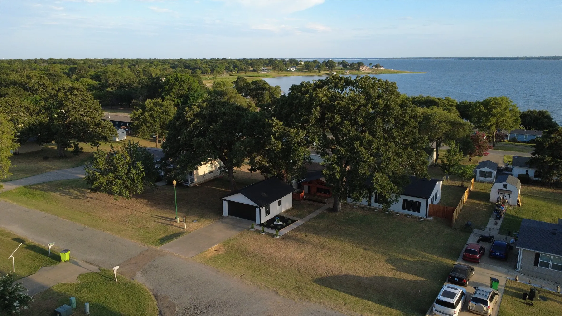 Waterfront community featuring mature trees, residential properties, and a paved street