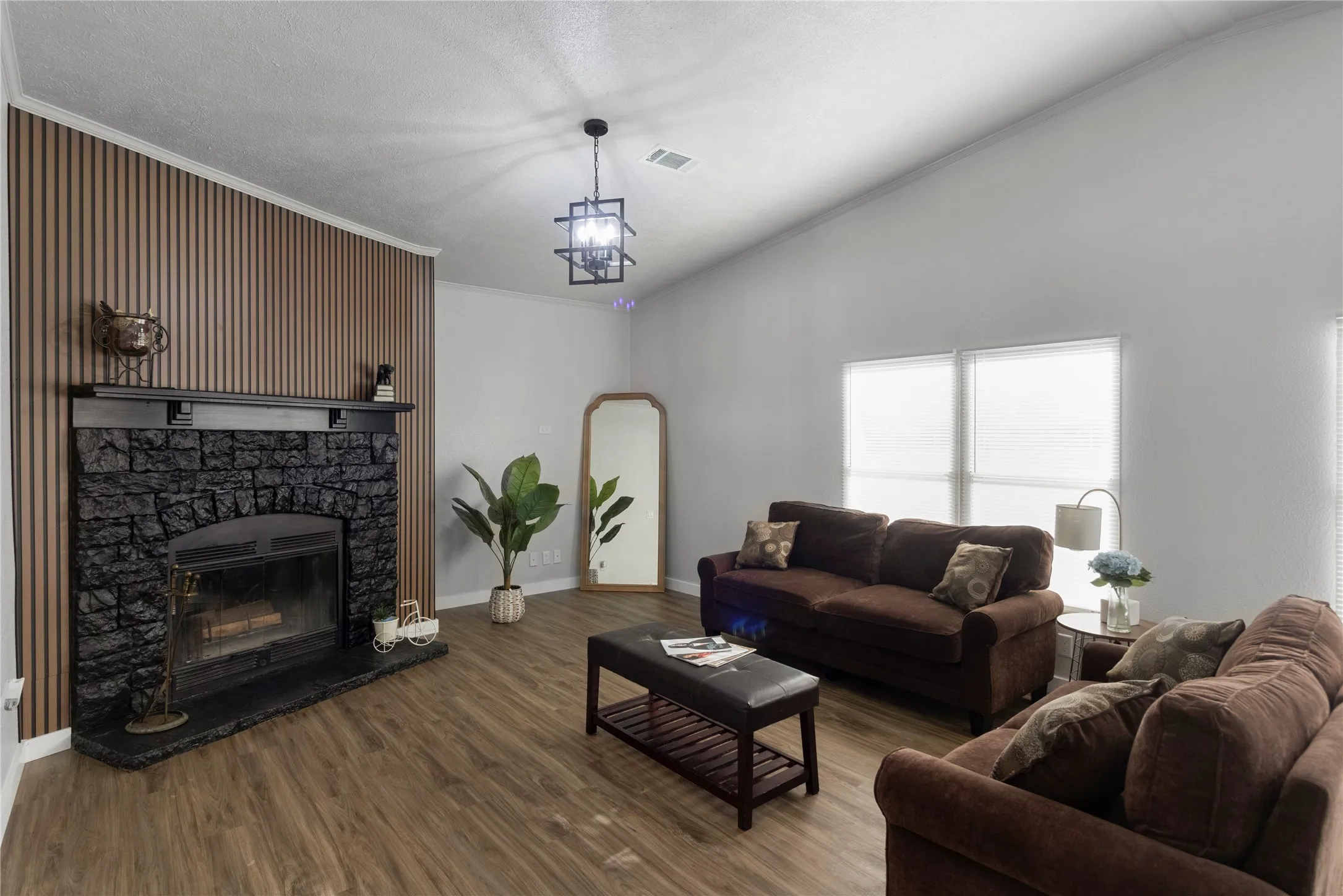 Living area featuring wood-finish flooring, a vaulted ceiling, and a prominent fireplace with a dark stone surround and a wood mantel