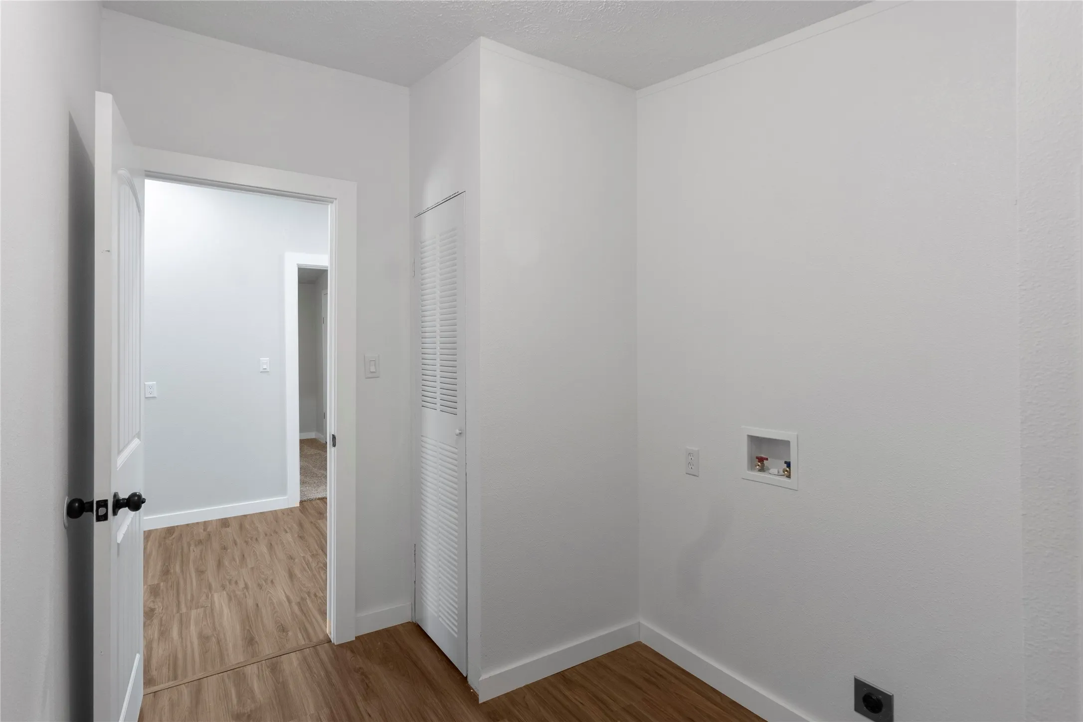 Dedicated laundry space featuring wood-finish flooring, white walls, and bifold louvered doors