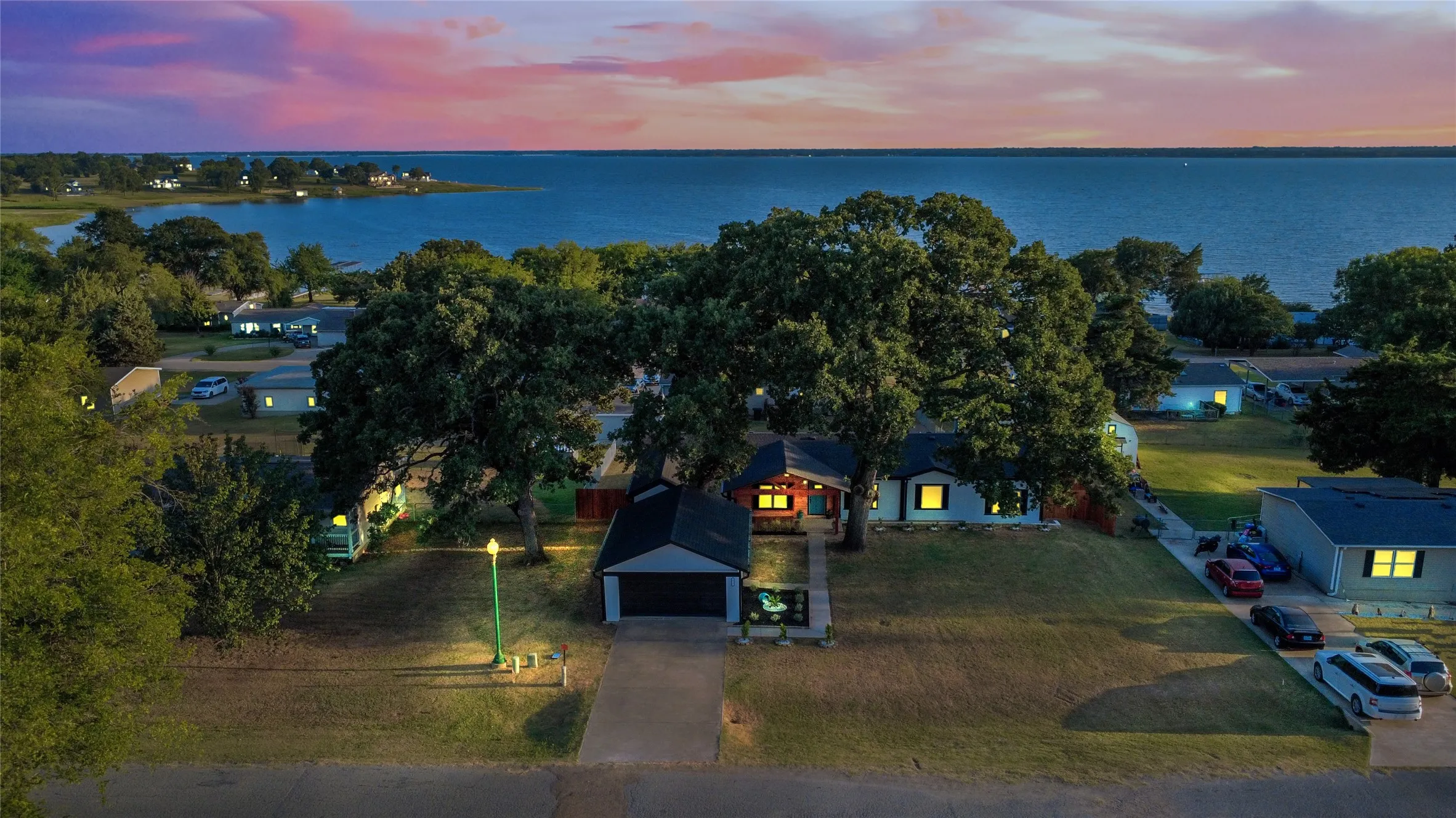 Waterfront neighborhood featuring a residential home with an attached garage, mature trees, and a paved driveway