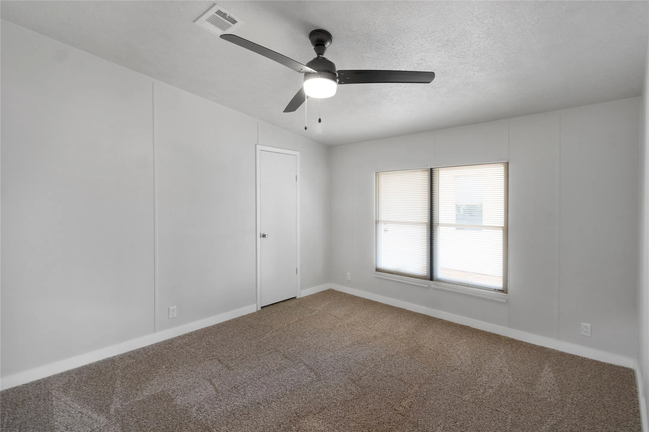 Room featuring neutral-toned carpet, light gray wall panels, white trim, and a contemporary ceiling fan with integrated lighting