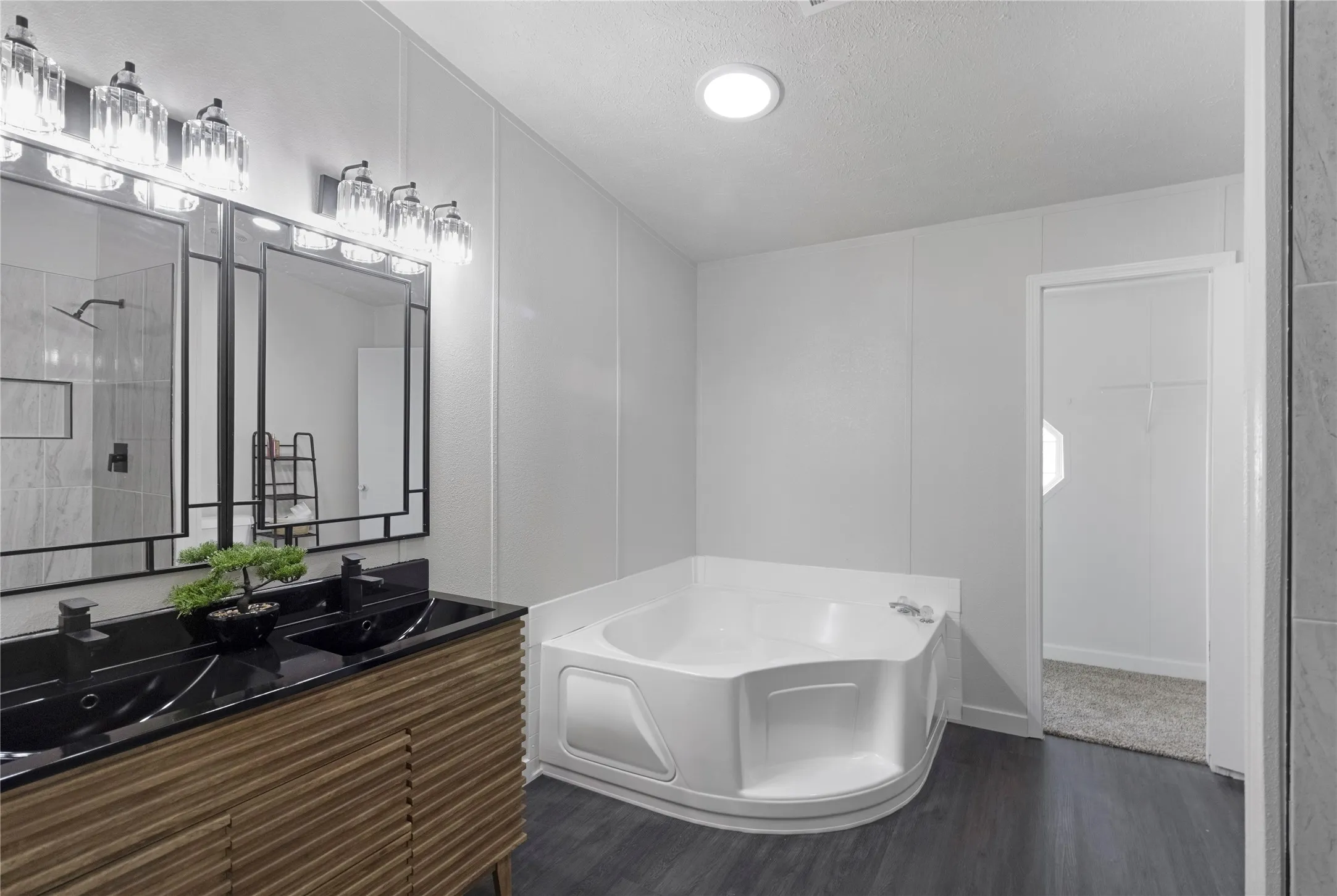 Bathroom featuring a corner soaking tub, a dual vanity with black countertops and sinks, and a separate shower with tile surround