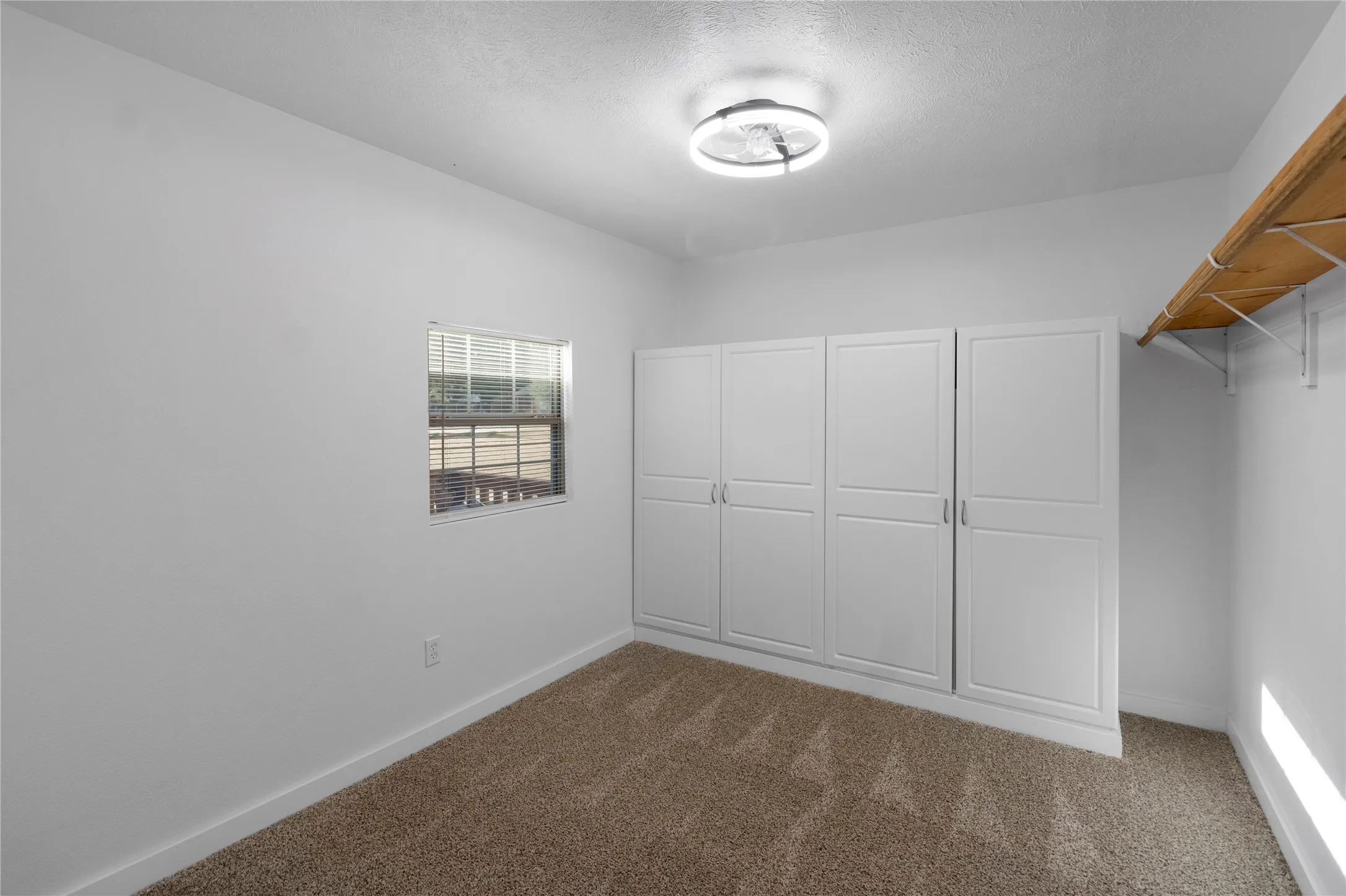 Huge master closet with white walls with a textured ceiling, a window with horizontal blinds, and built-in white cabinetry featuring panel doors