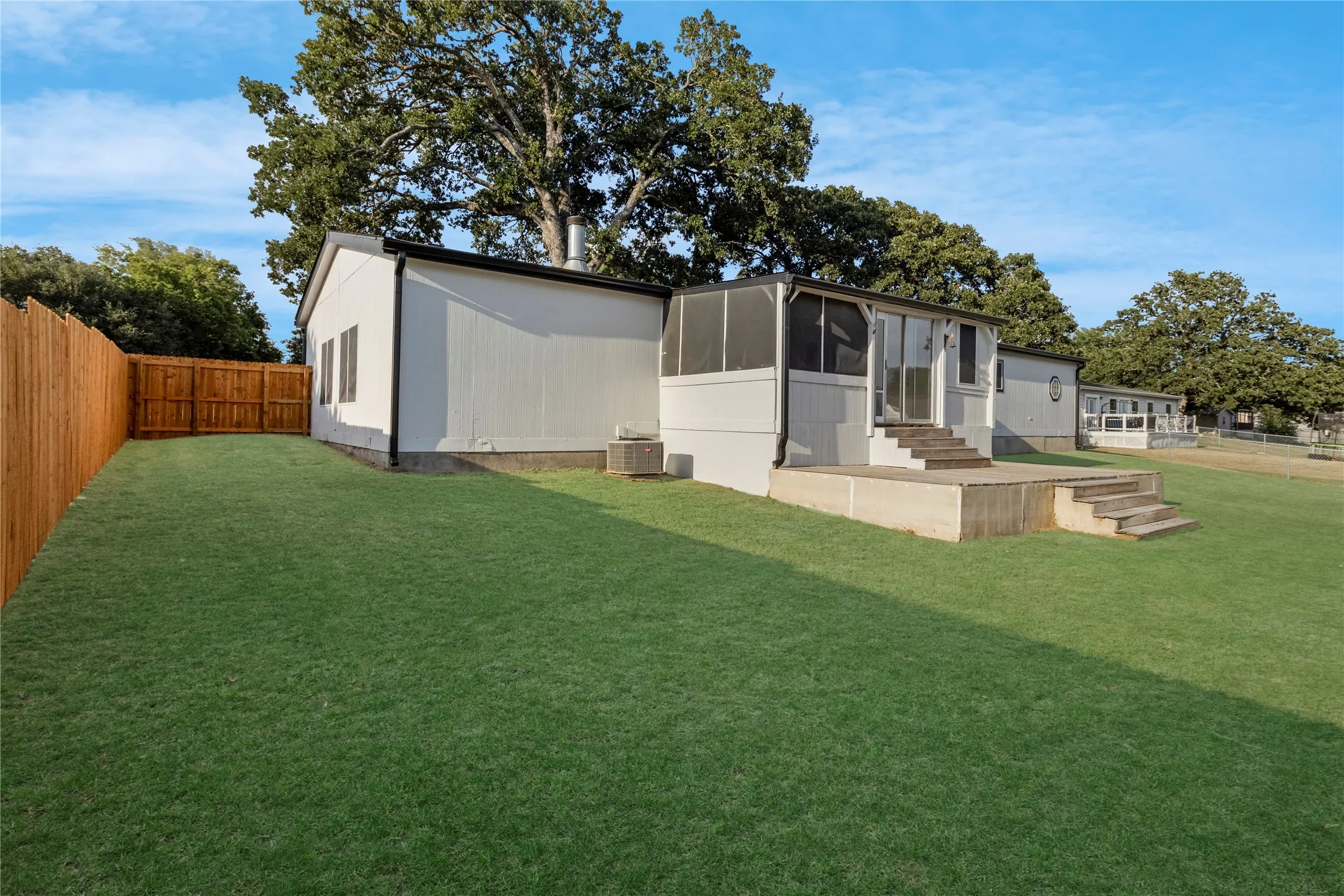 Spacious backyard featuring a manicured lawn, wood fencing, concrete patio with steps, and a screened porch