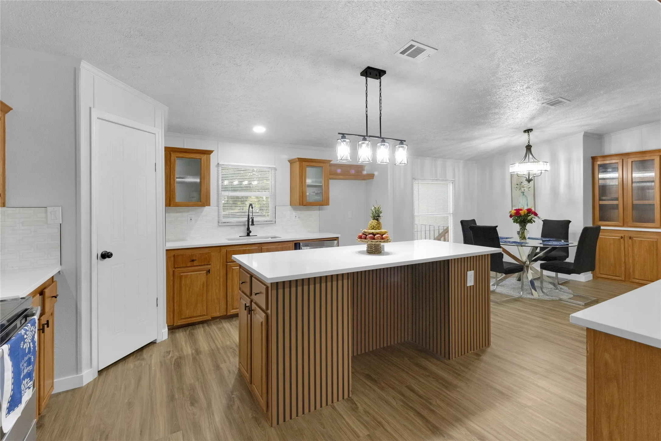 Kitchen featuring a central island with slat wood paneling and white countertop, wood-finish flooring, recessed lighting, and a chandelier over the dining area