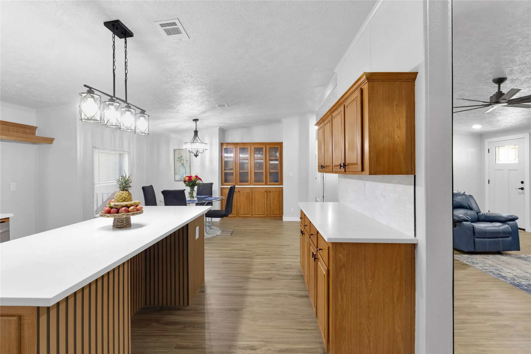 Kitchen island with white countertop, slatted wood-finish paneling, and a contemporary chandelier