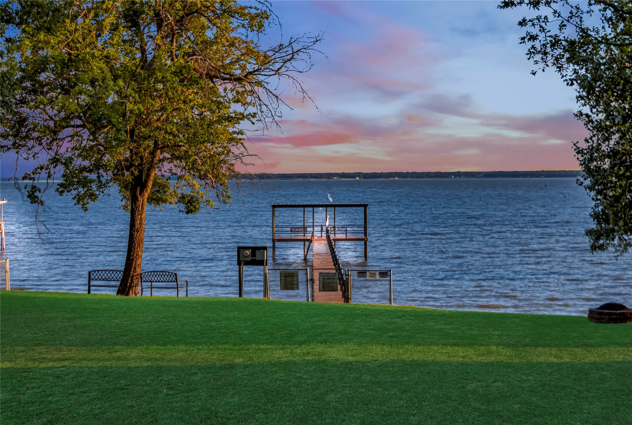 Waterfront neighborhood park featuring a private two-story boat dock with a walkway, expansive green lawn, and mature trees