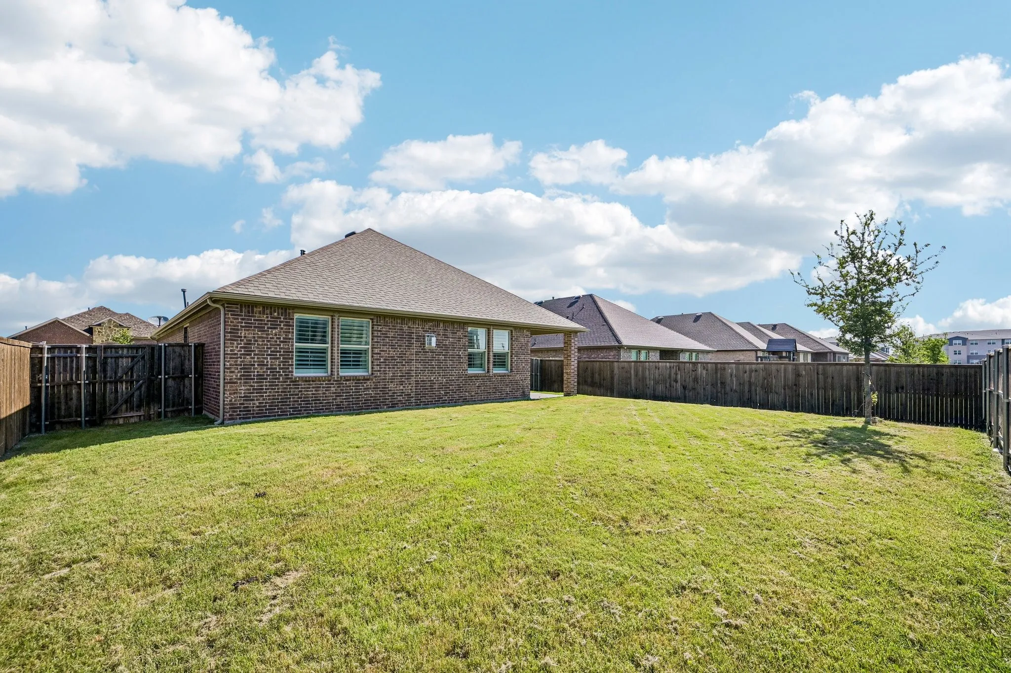 Spacious rear yard with a manicured lawn, full privacy fencing, and brick exterior
