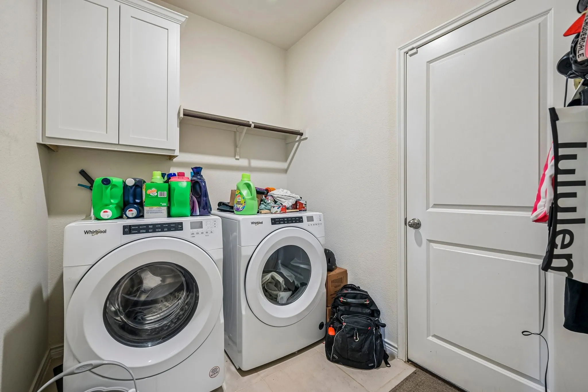 Dedicated utility area featuring white shaker-style upper cabinetry and an open wall shelf