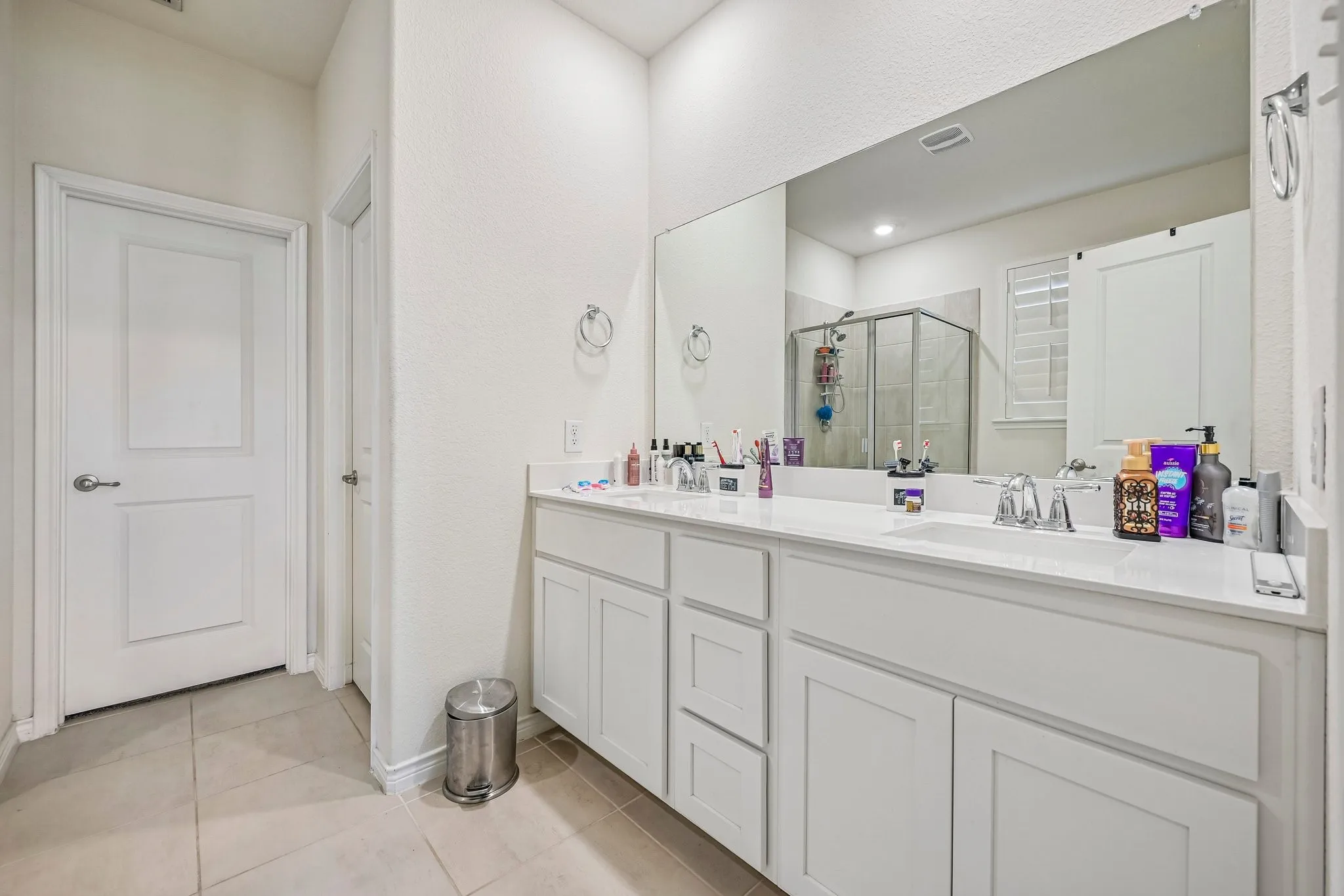Bathroom featuring a dual vanity with white cabinetry and a light-toned countertop, a frameless mirror spanning the vanity, and a glass-enclosed shower