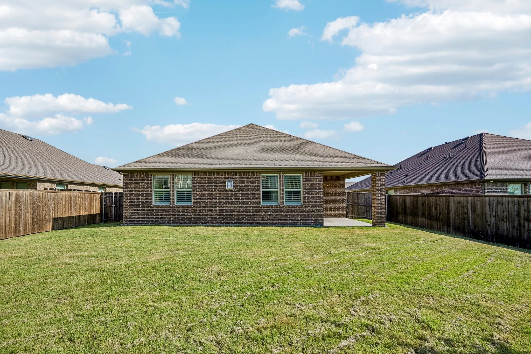 Expansive backyard featuring a manicured lawn, full privacy fencing, and a covered concrete patio