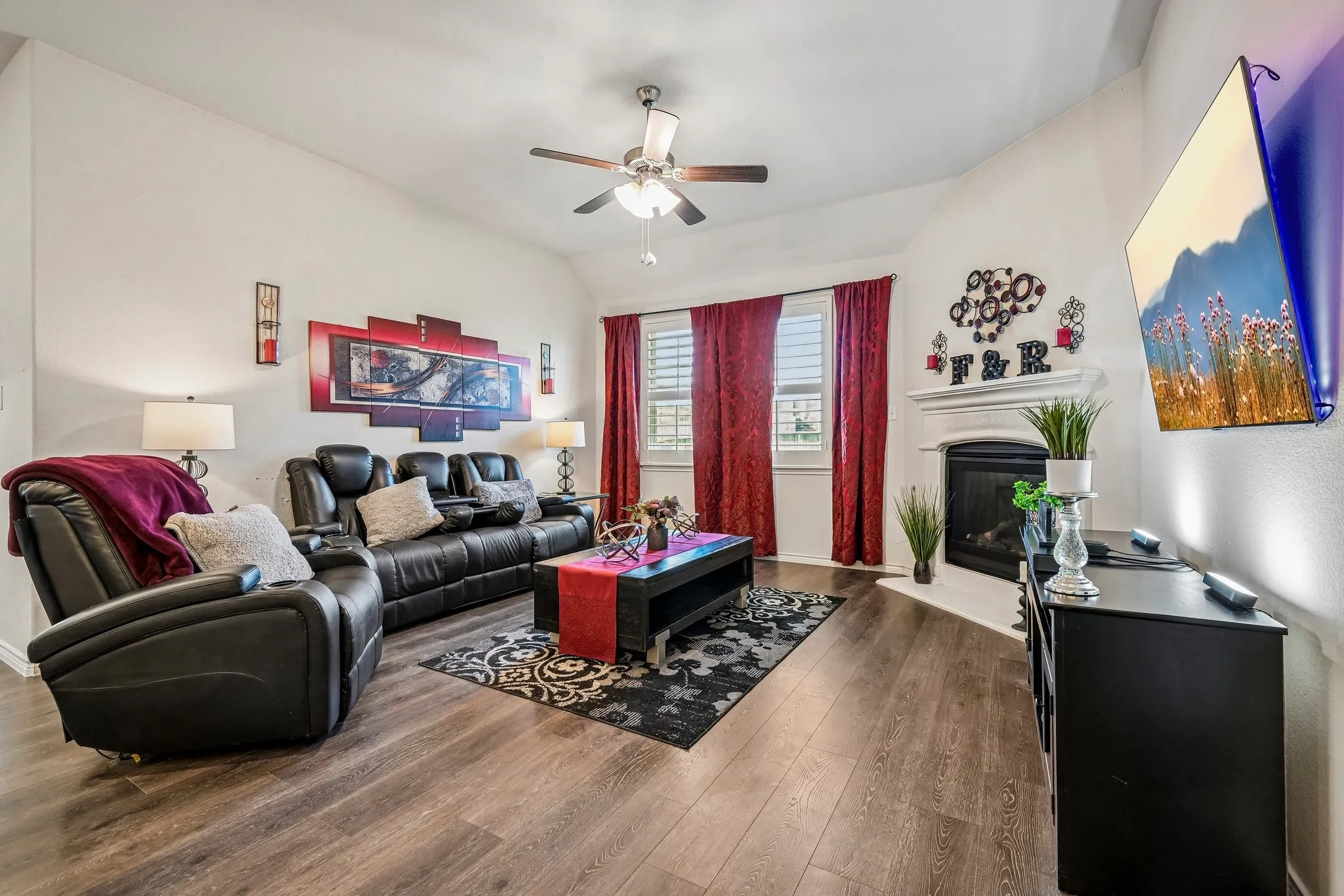 Living area with vaulted ceilings, wood-finish flooring, a corner fireplace with a white mantel, and a ceiling fan