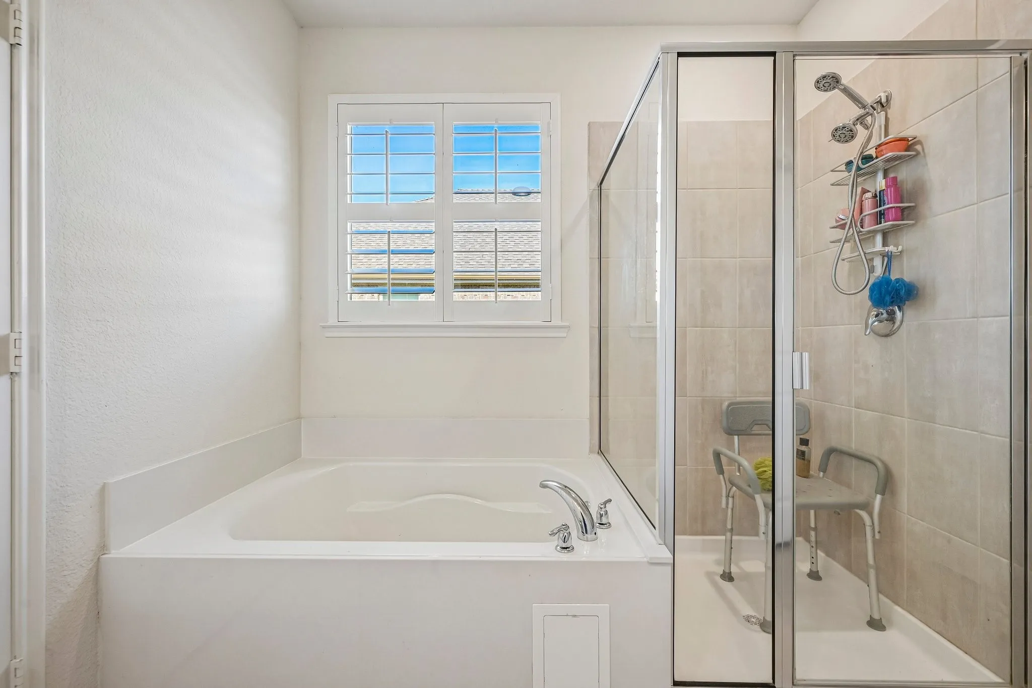Soaking tub with deck-mounted chrome faucet, accompanied by a separate glass-enclosed shower with tile surround and multiple shower heads